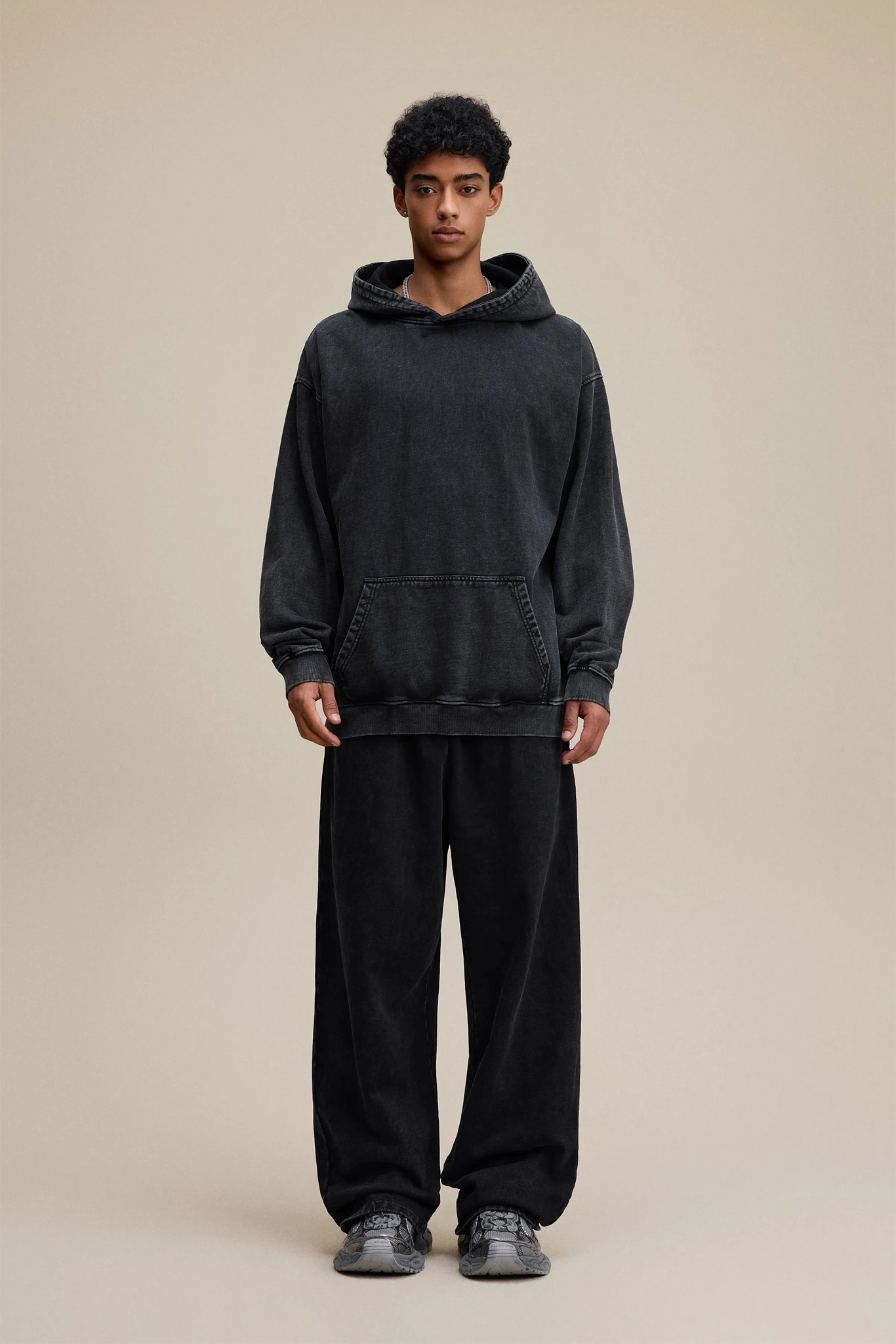 Person wearing a black hoodie and pants on a beige background