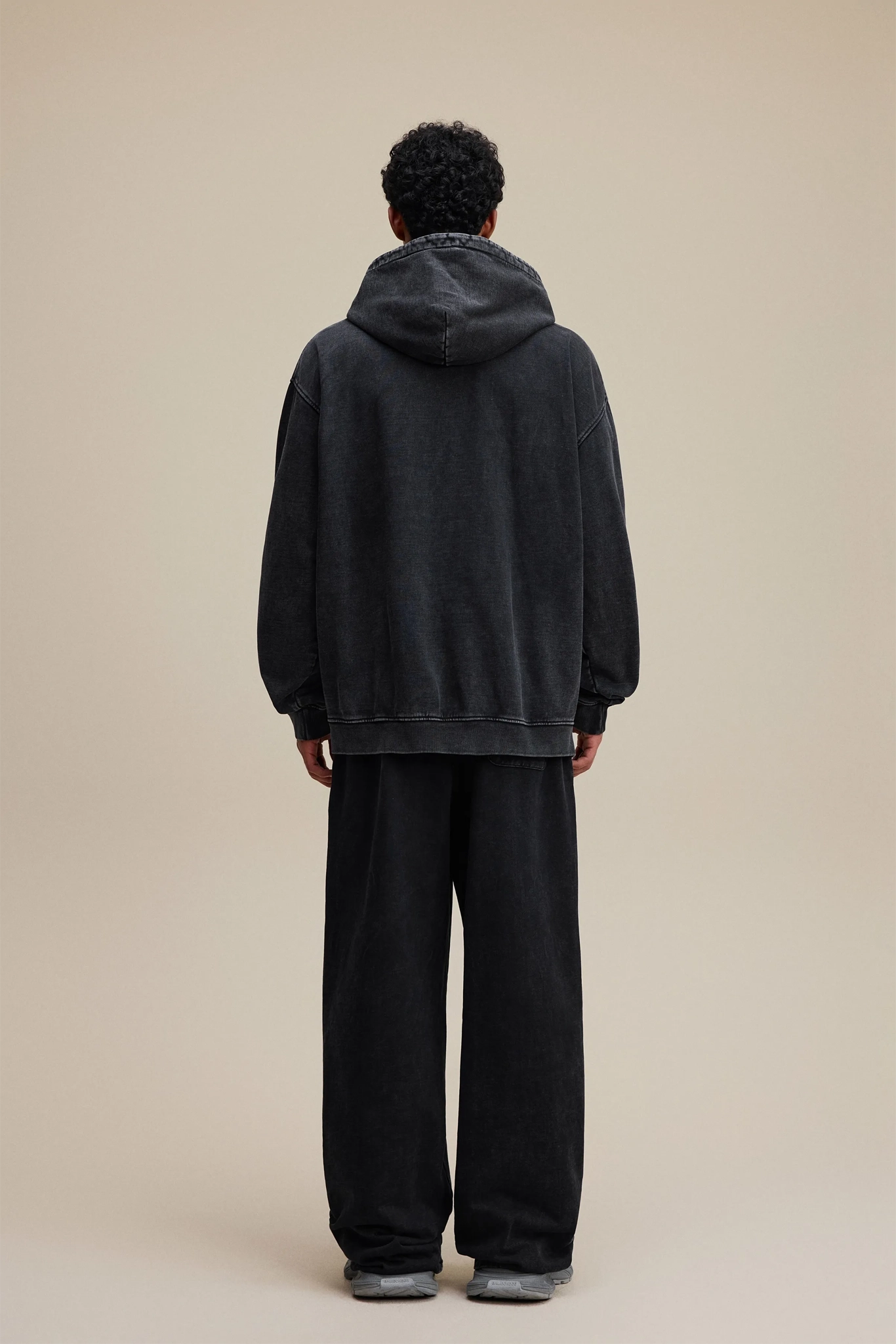 Person wearing a black hoodie and pants on a beige background