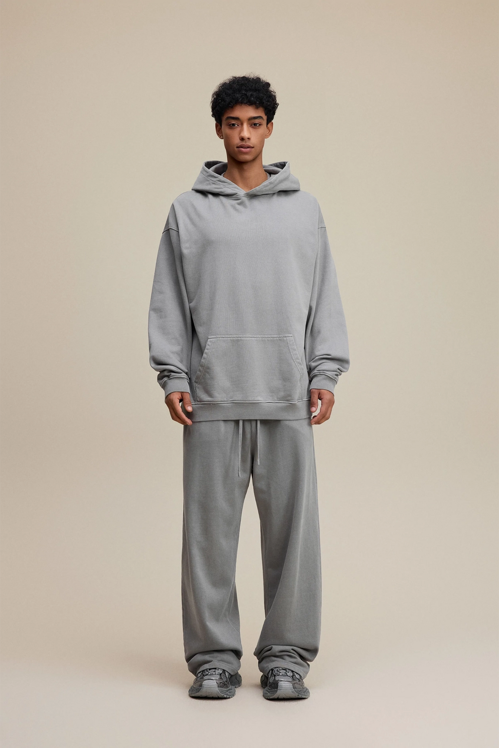 Person wearing a gray hoodie and pants on a beige background