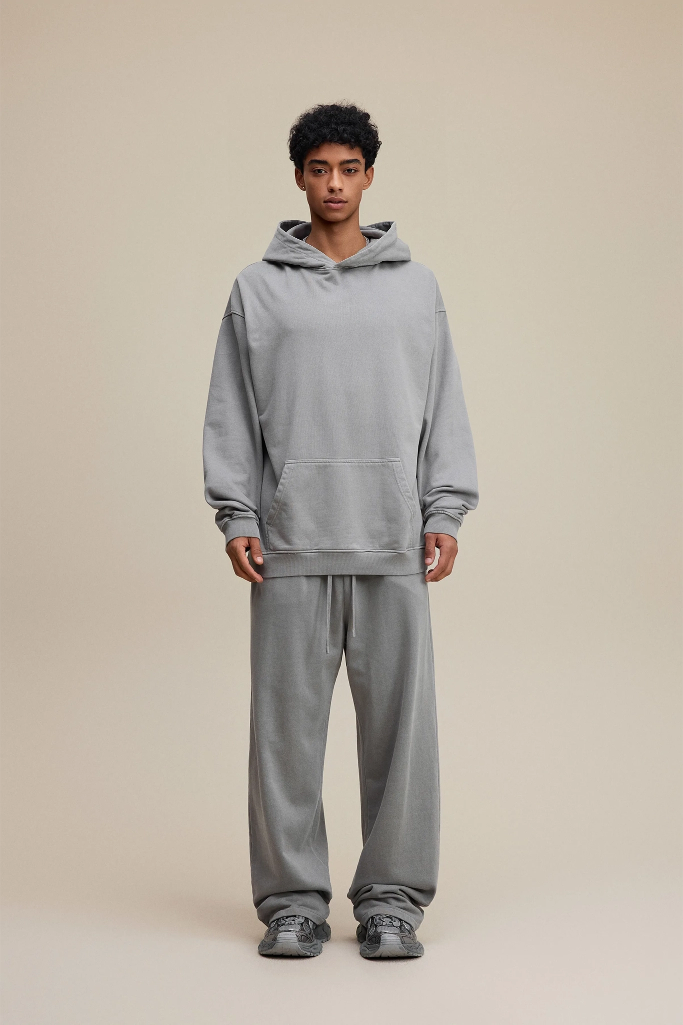 Person wearing a gray hoodie and pants on a beige background