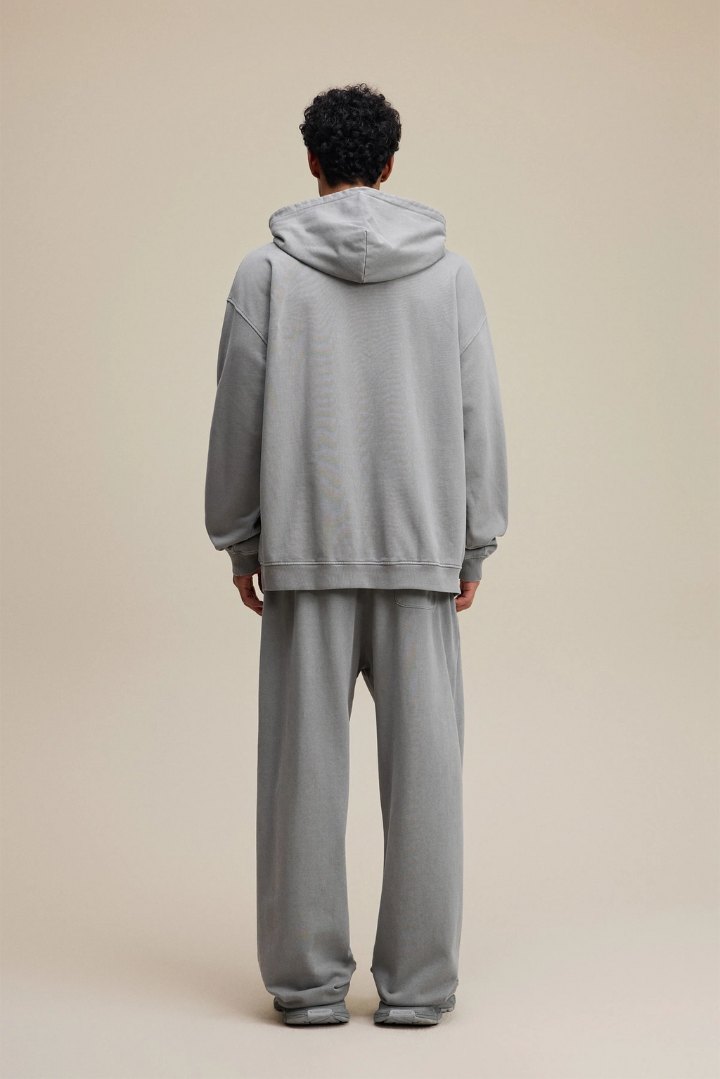 Person wearing a gray tracksuit against a beige background