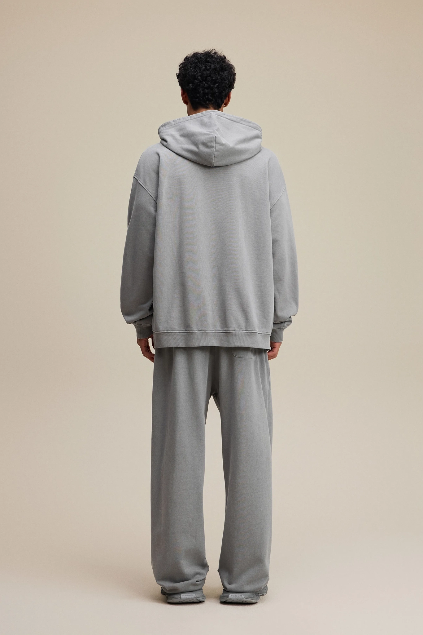 Person wearing a gray tracksuit against a beige background