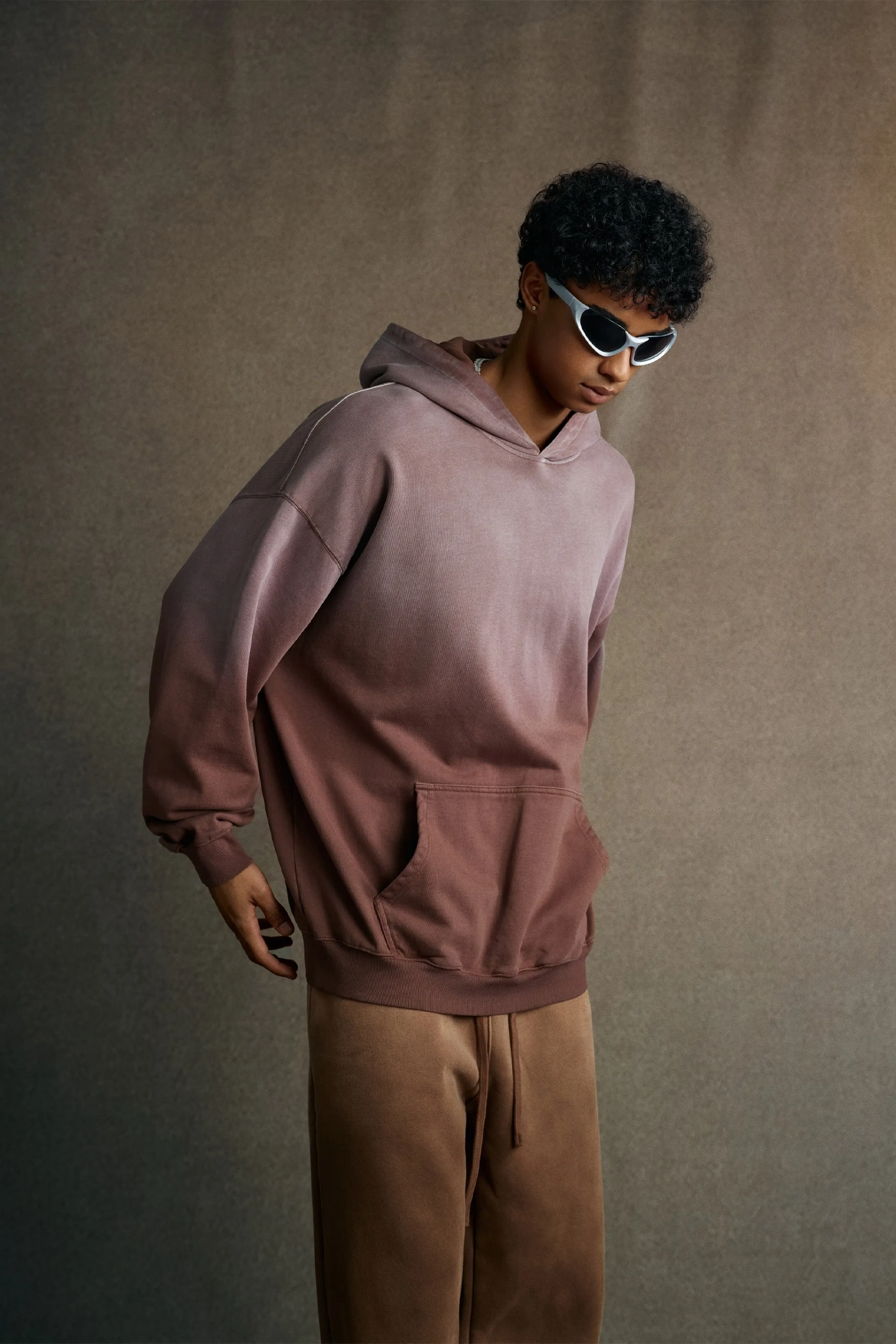 Person wearing a pink hoodie and brown pants against a plain background