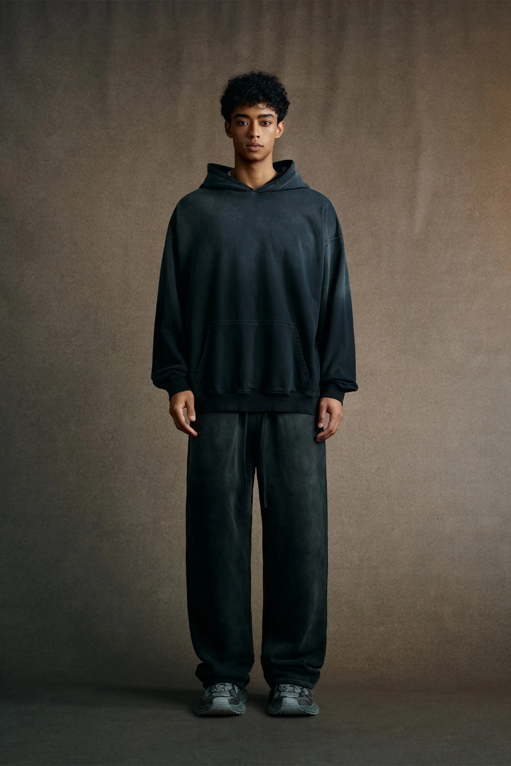 Person wearing a dark hoodie and pants against a plain background