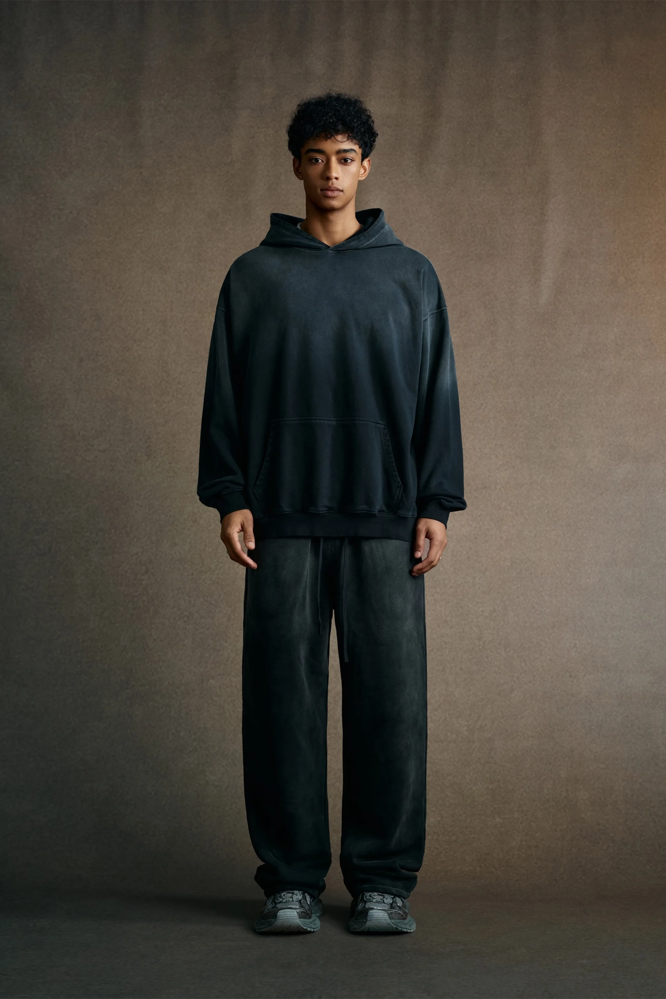 Person wearing a dark hoodie and pants against a plain background