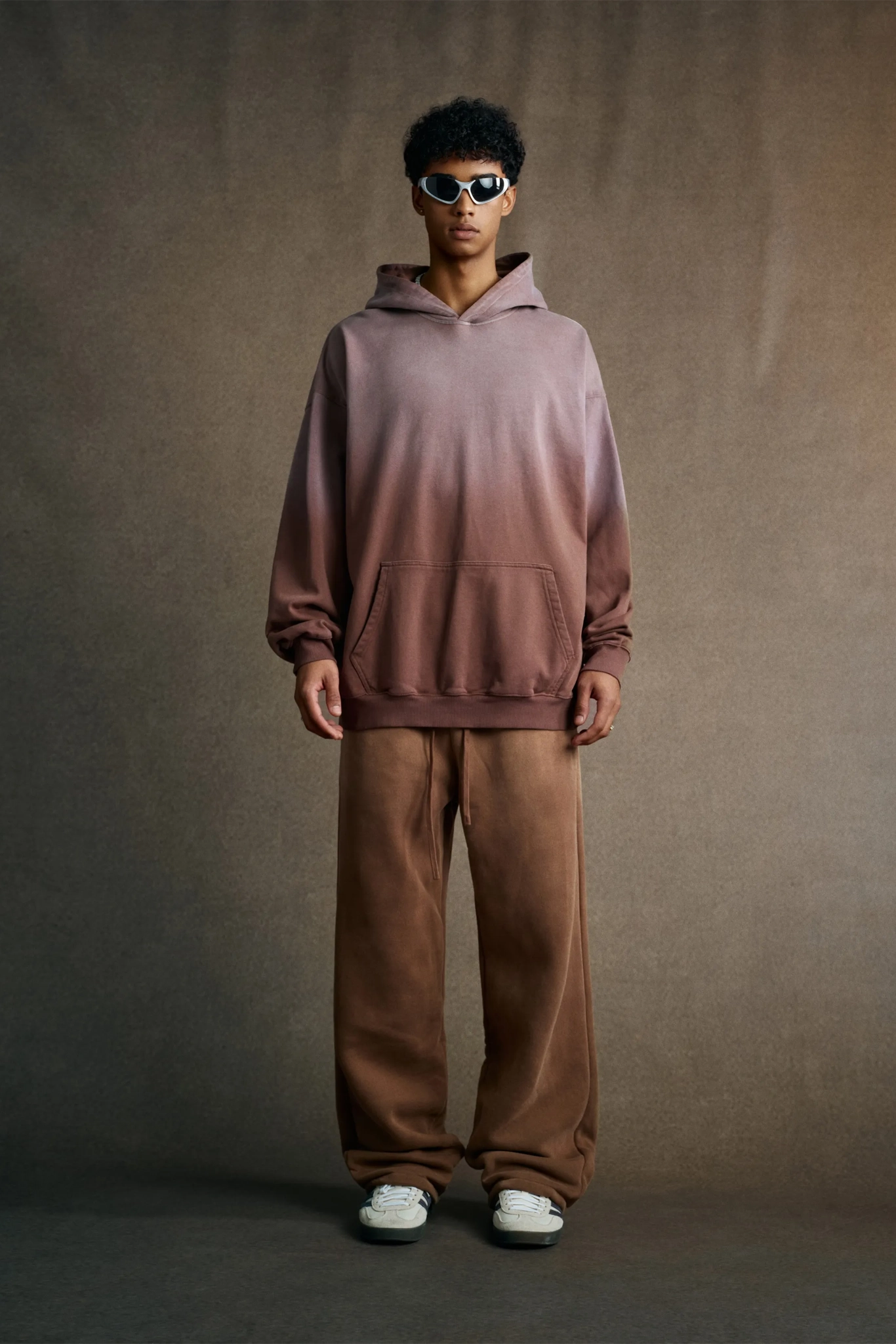 Person wearing a gradient hoodie and brown pants against a plain background