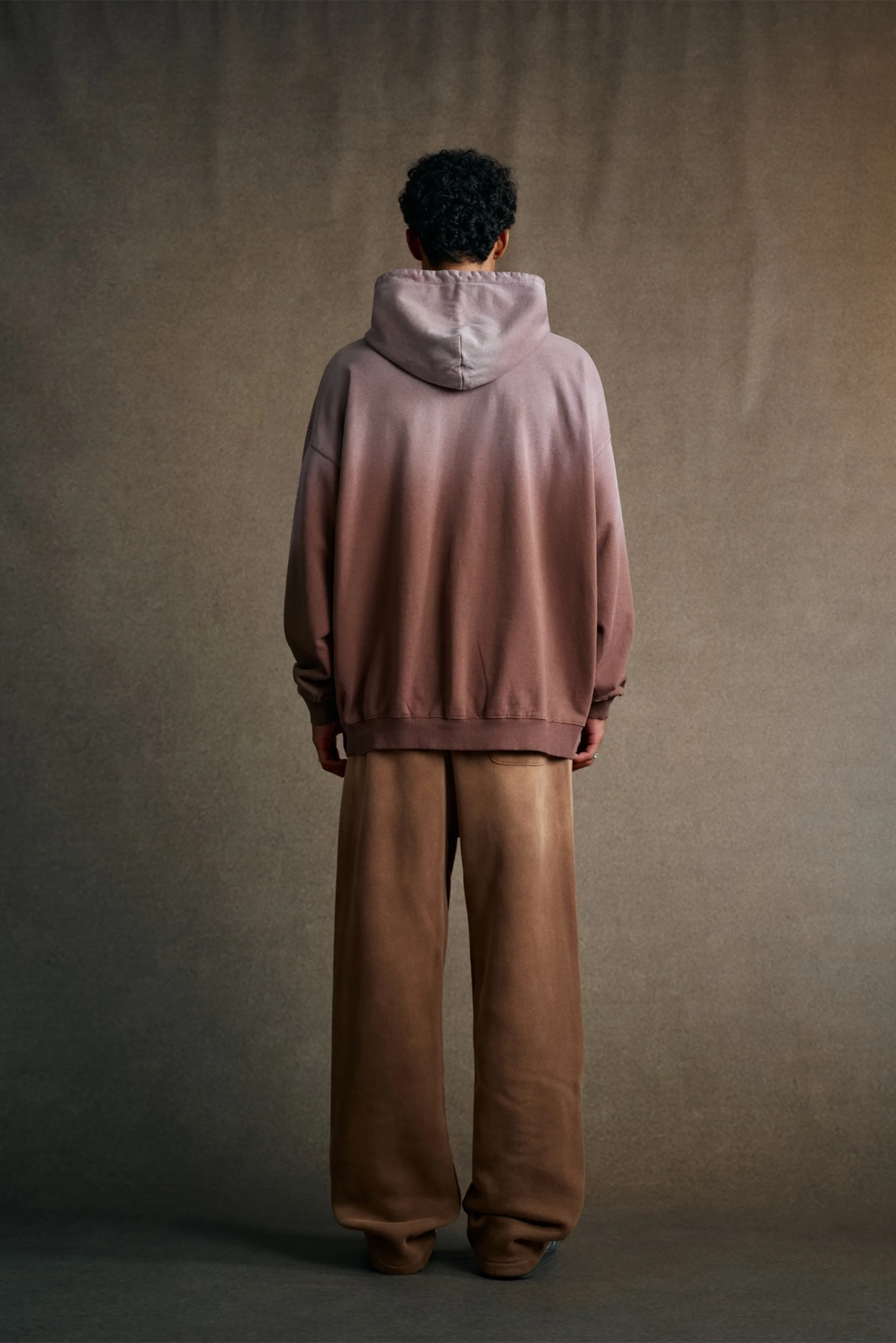 Person wearing a gradient hoodie and brown pants against a plain background