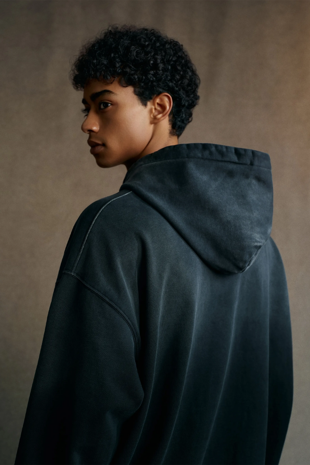 Person wearing a dark hoodie against a neutral background