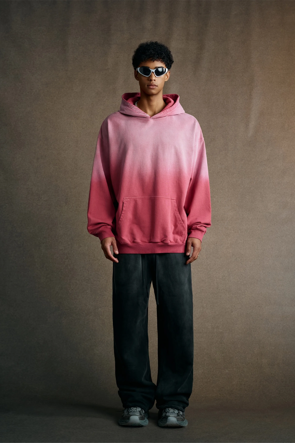 Person wearing a pink gradient hoodie against a brown background
