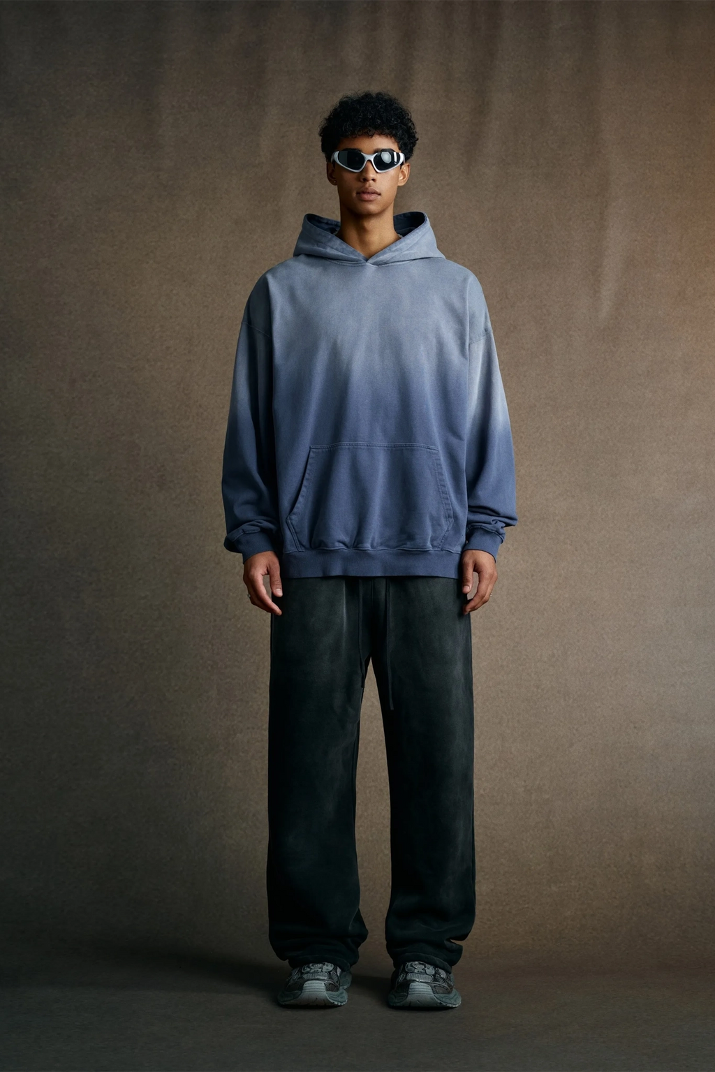 Person wearing a blue hoodie and dark pants against a brown background