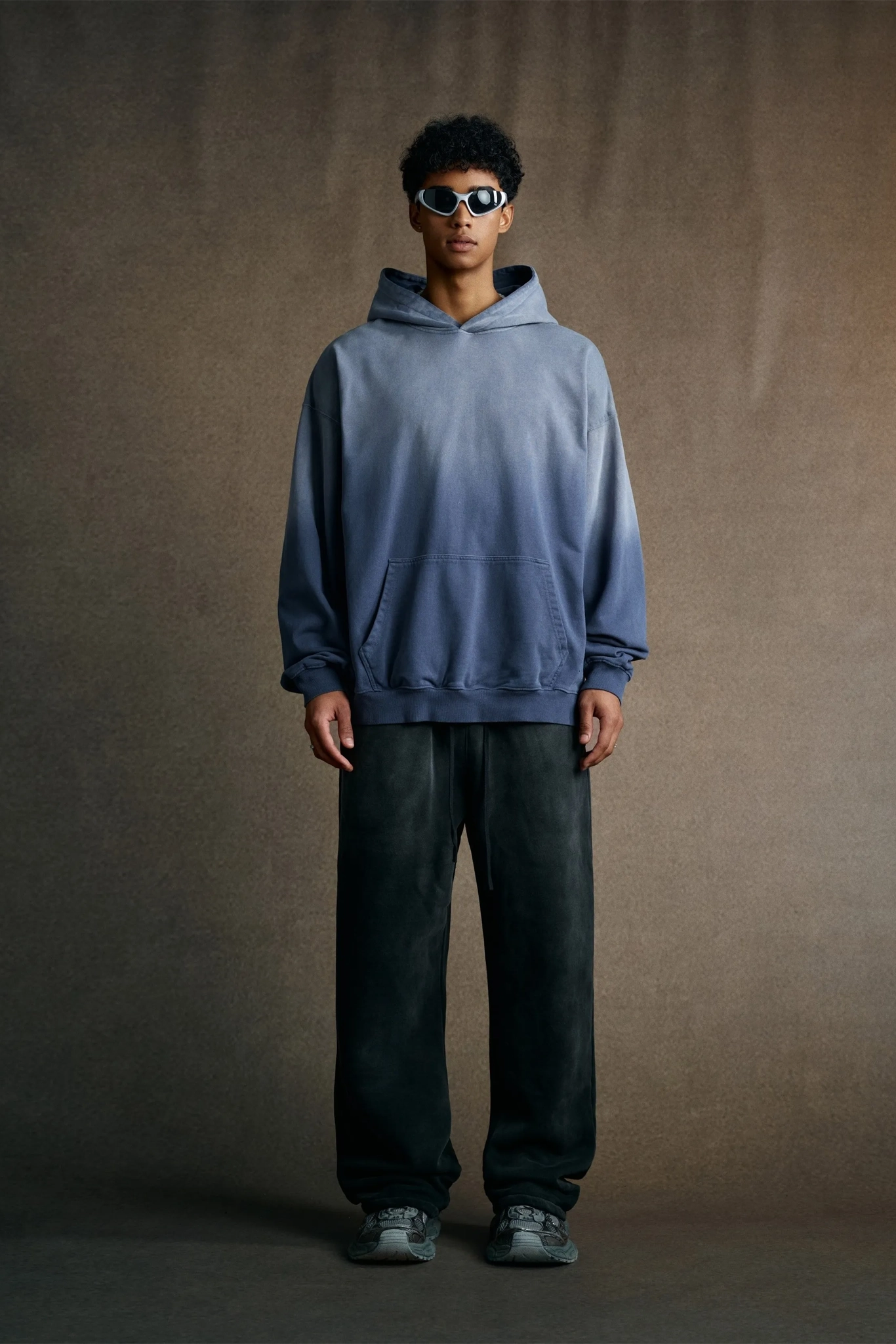 Person wearing a blue hoodie and dark pants against a brown background