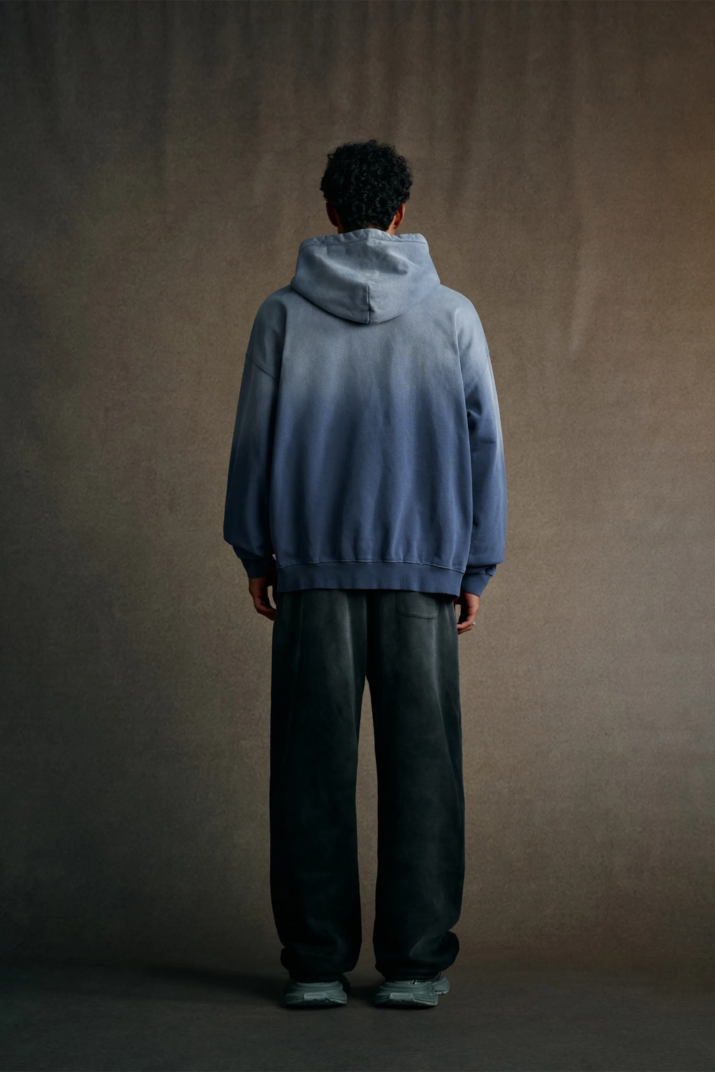 Person wearing a blue hoodie and dark pants standing against a plain background