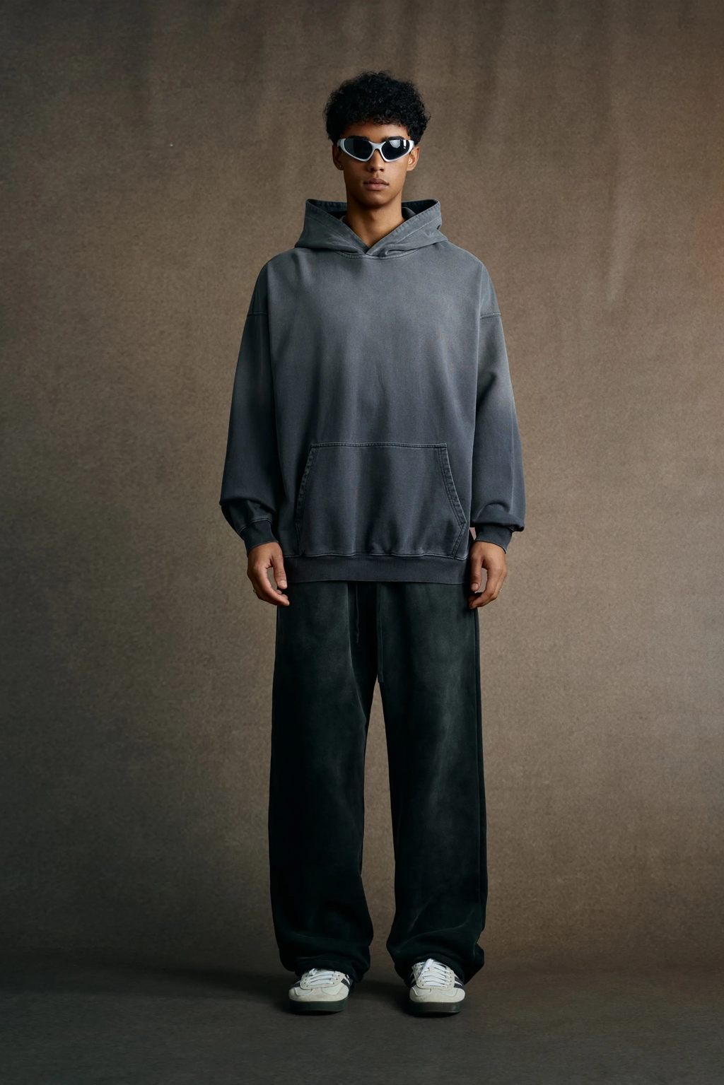 Person wearing a gray hoodie and dark pants against a brown background