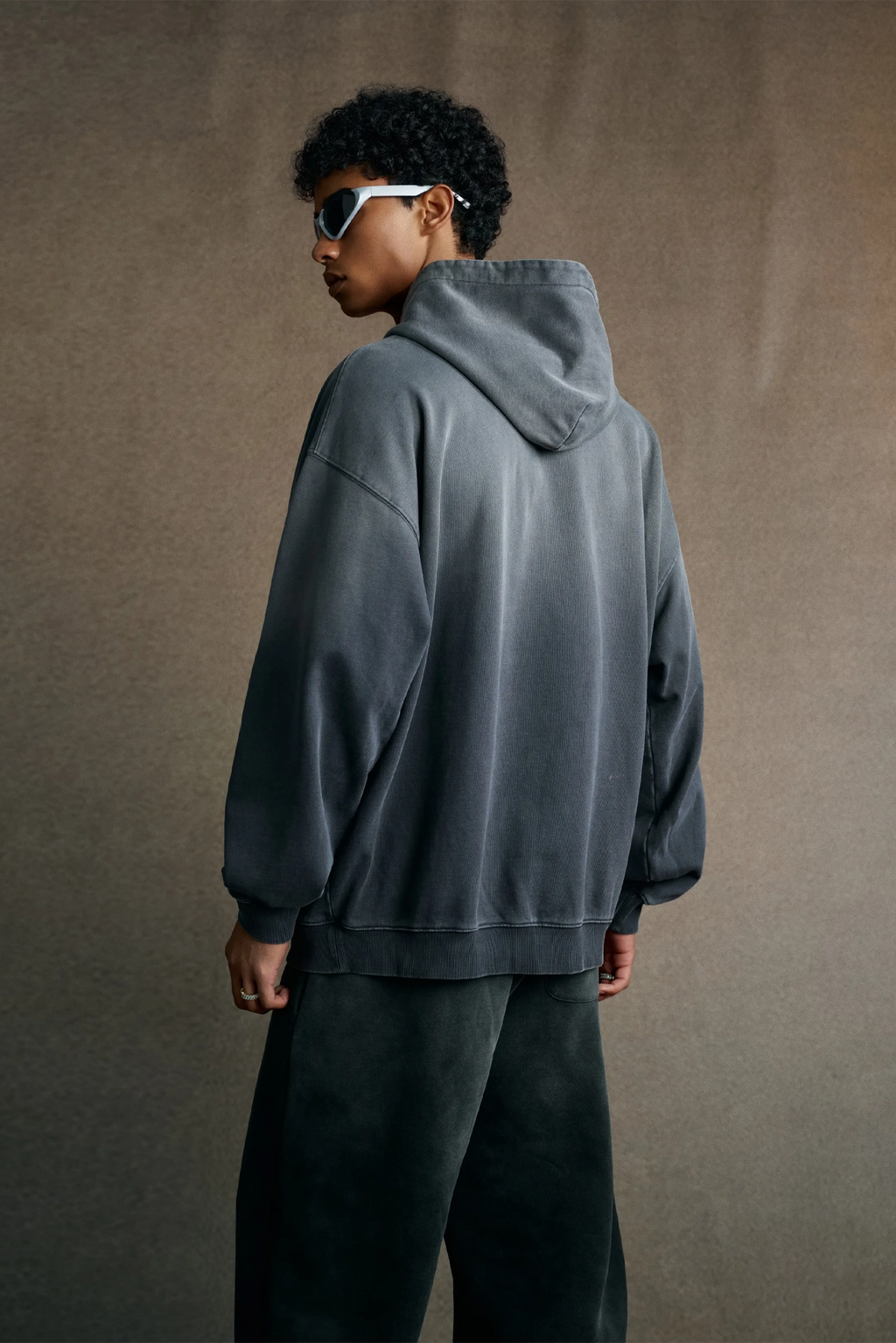 Person wearing a gray hoodie and dark pants against a brown background