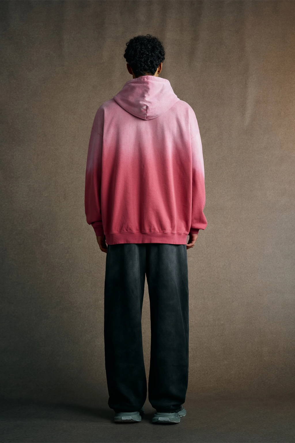 Person wearing a pink gradient hoodie against a brown background