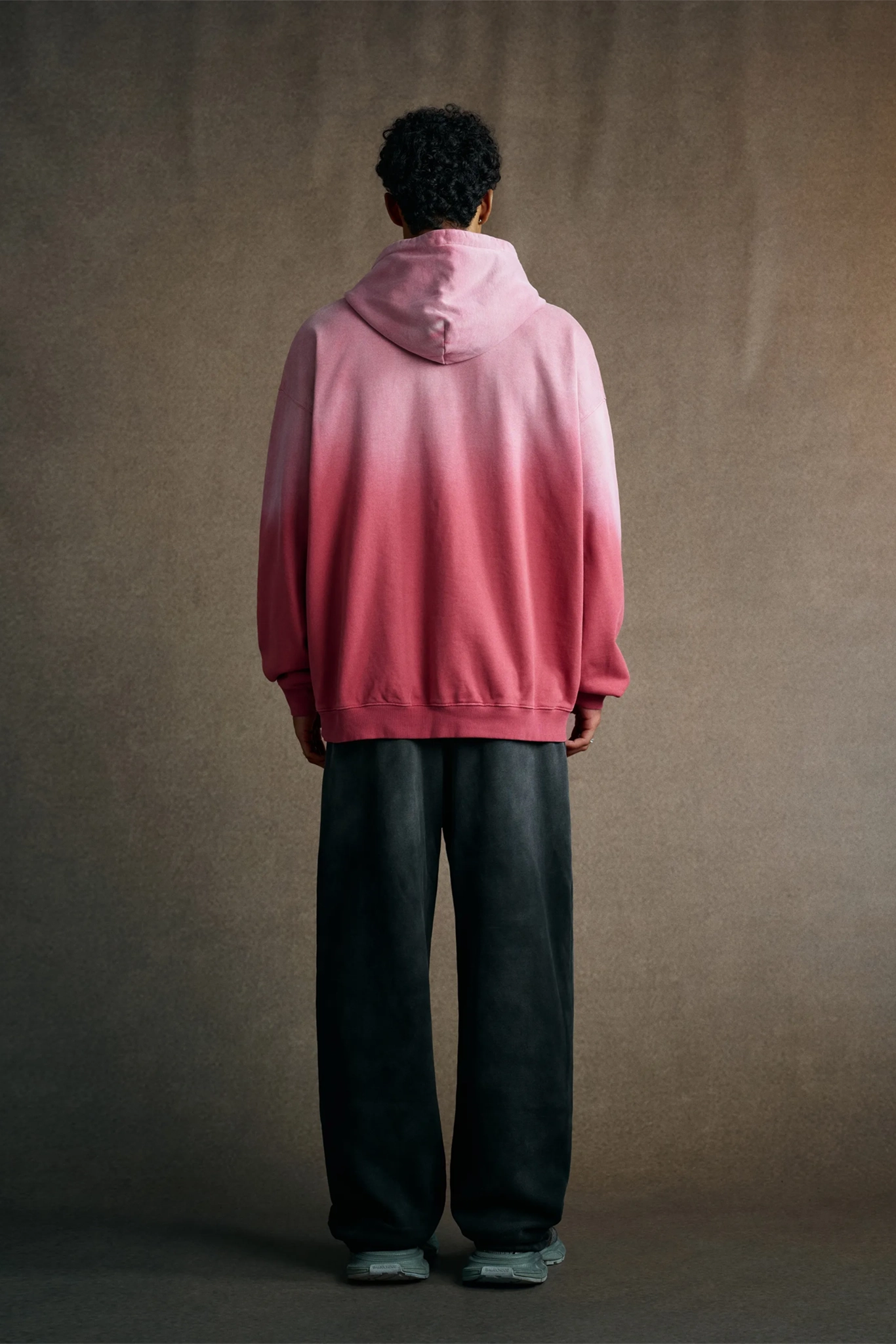 Person wearing a pink gradient hoodie against a brown background