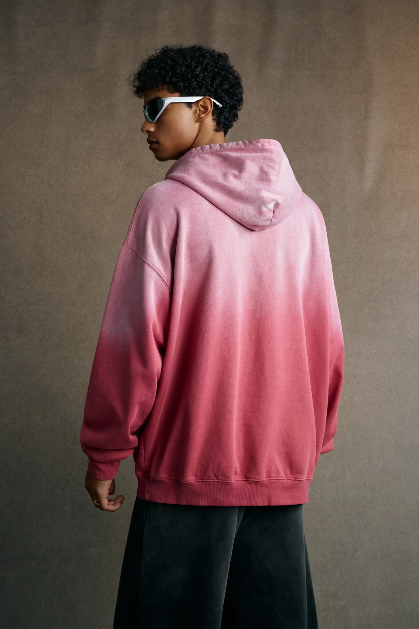 Person wearing a pink gradient hoodie against a plain background