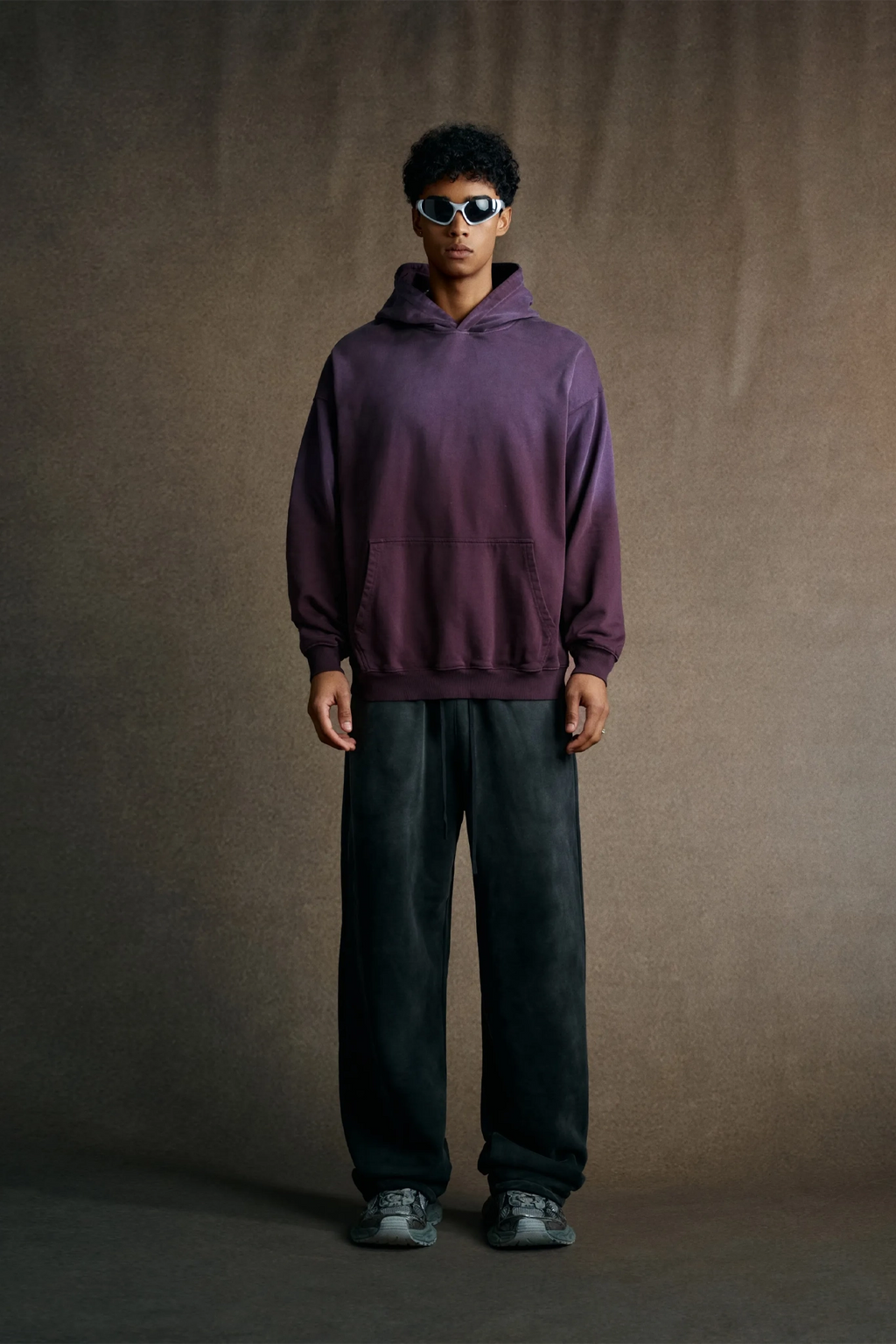 Person wearing a purple hoodie and dark pants against a brown background