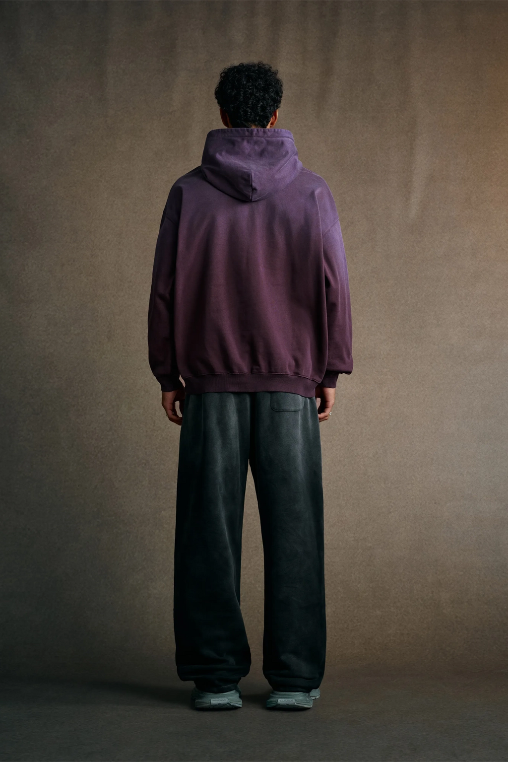 Person wearing a purple hoodie and dark pants standing against a plain background
