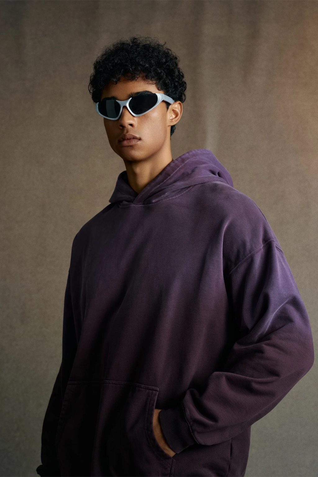 Person wearing a purple hoodie and sunglasses against a neutral background