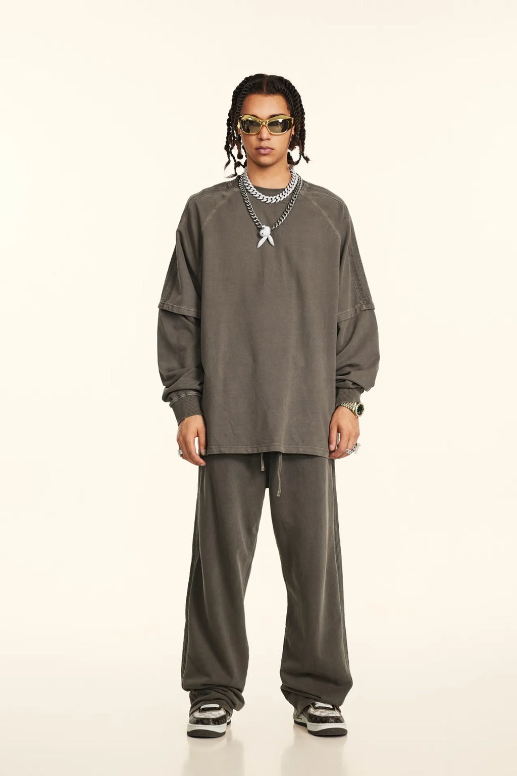 Person wearing a gray outfit with sunglasses on a white background