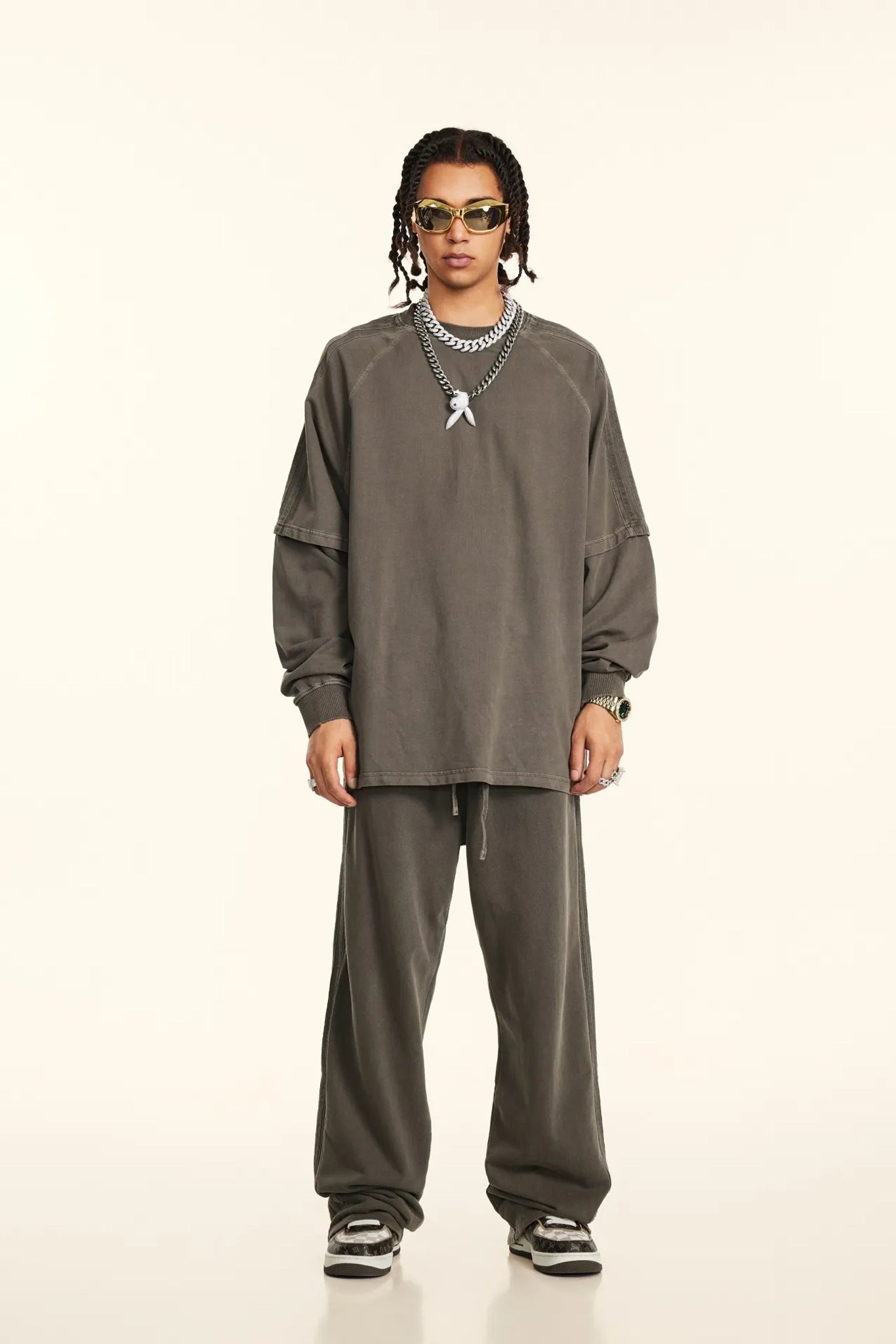 Person wearing a gray outfit with sunglasses on a white background