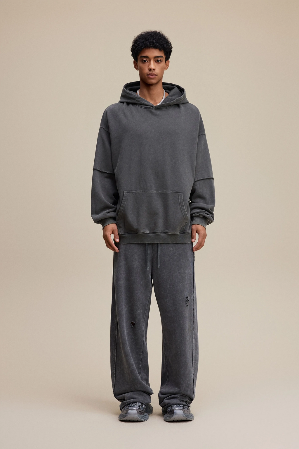 Person wearing a gray hoodie and pants on a beige background