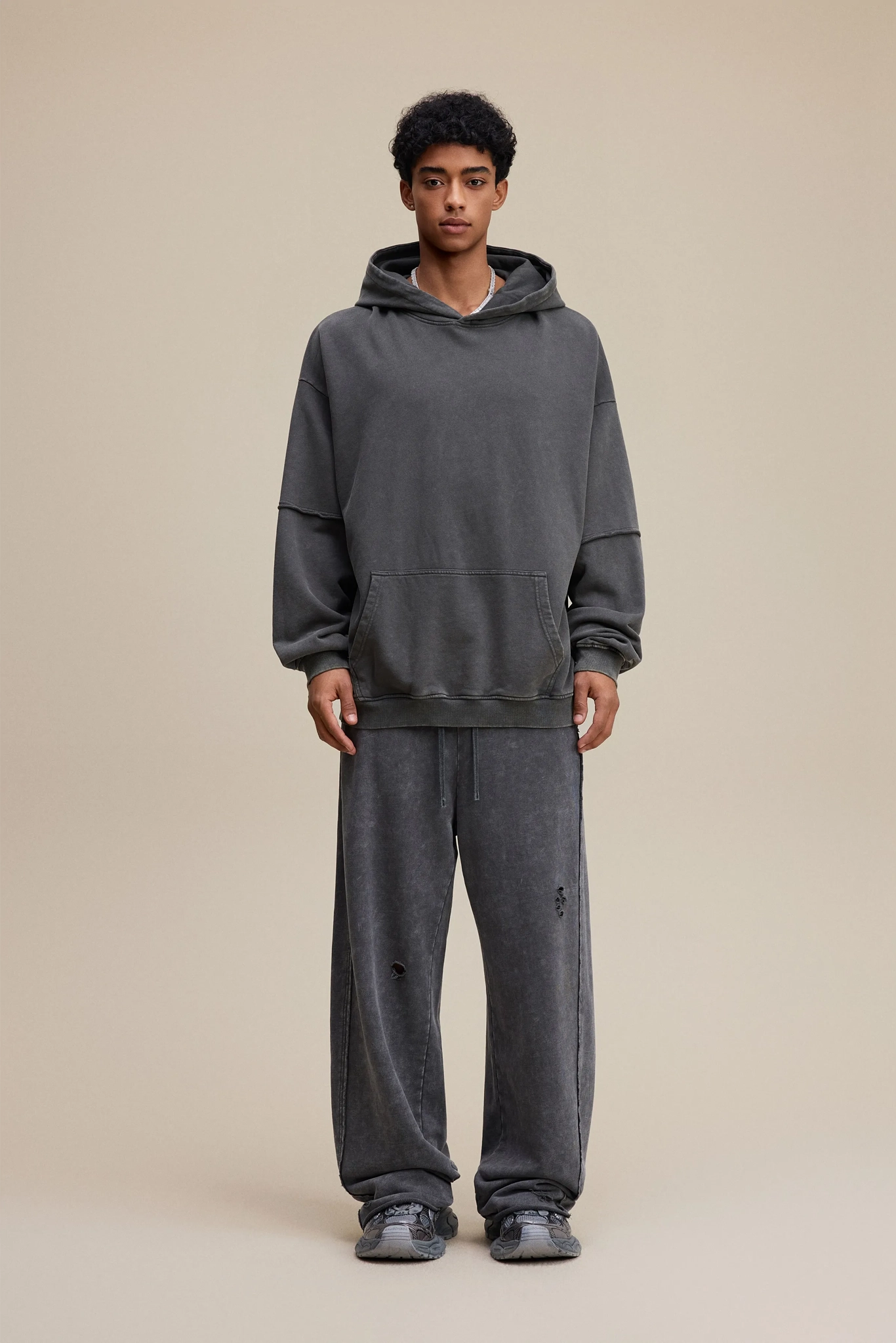 Person wearing a gray hoodie and pants on a beige background