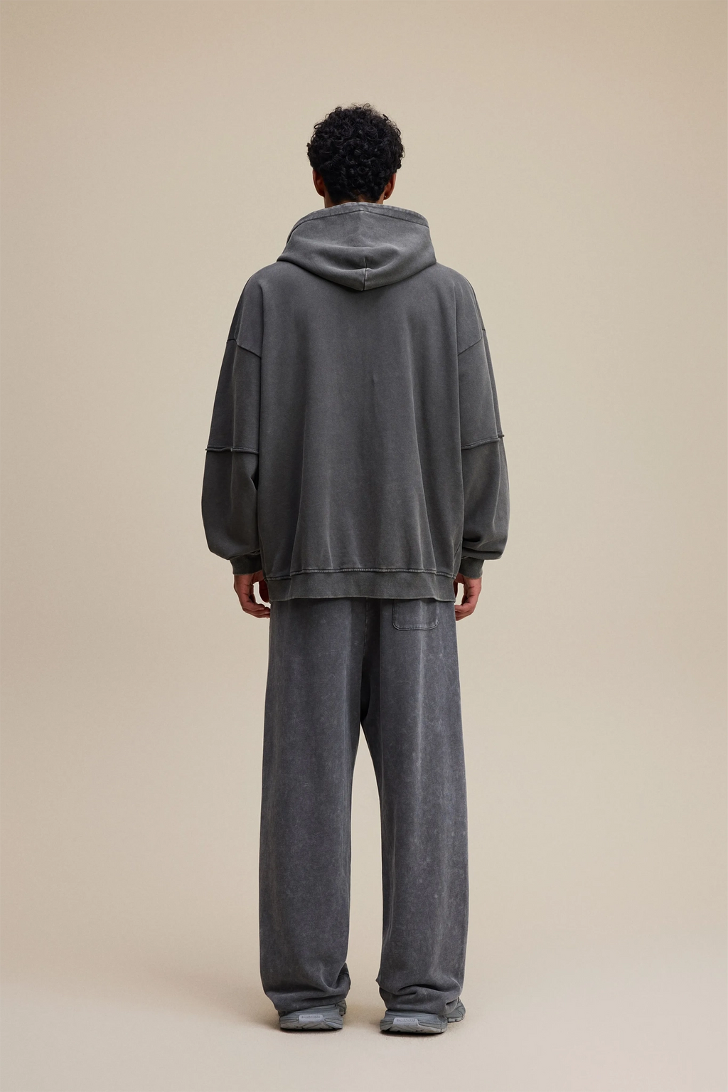 Person wearing a gray hoodie and pants on a beige background