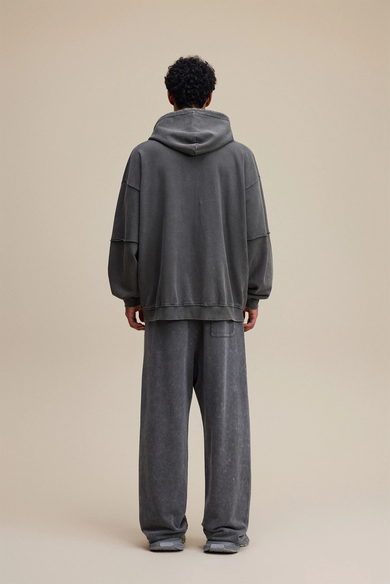 Person wearing a gray hoodie and pants on a beige background