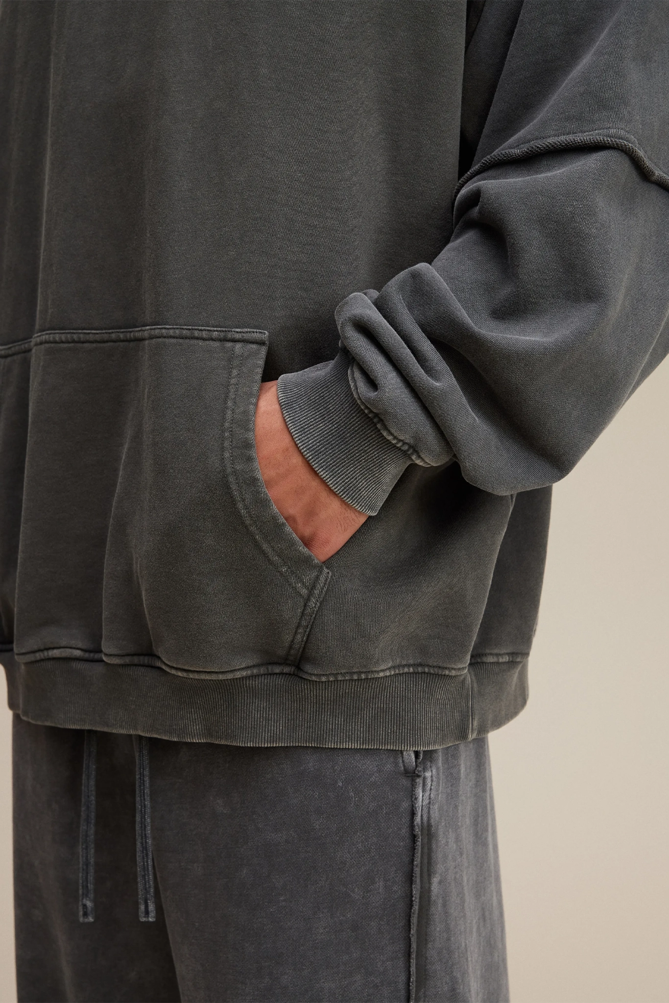 Person wearing a dark gray sweatshirt with a pocket, standing against a neutral background.