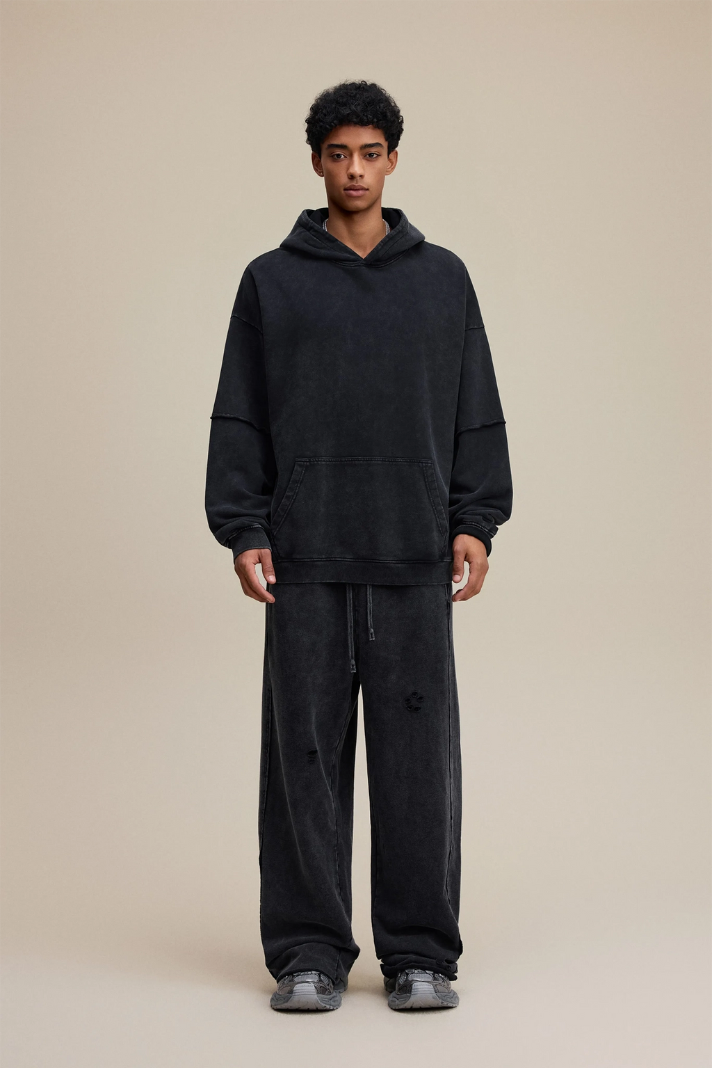 Person wearing a black hoodie and pants on a beige background