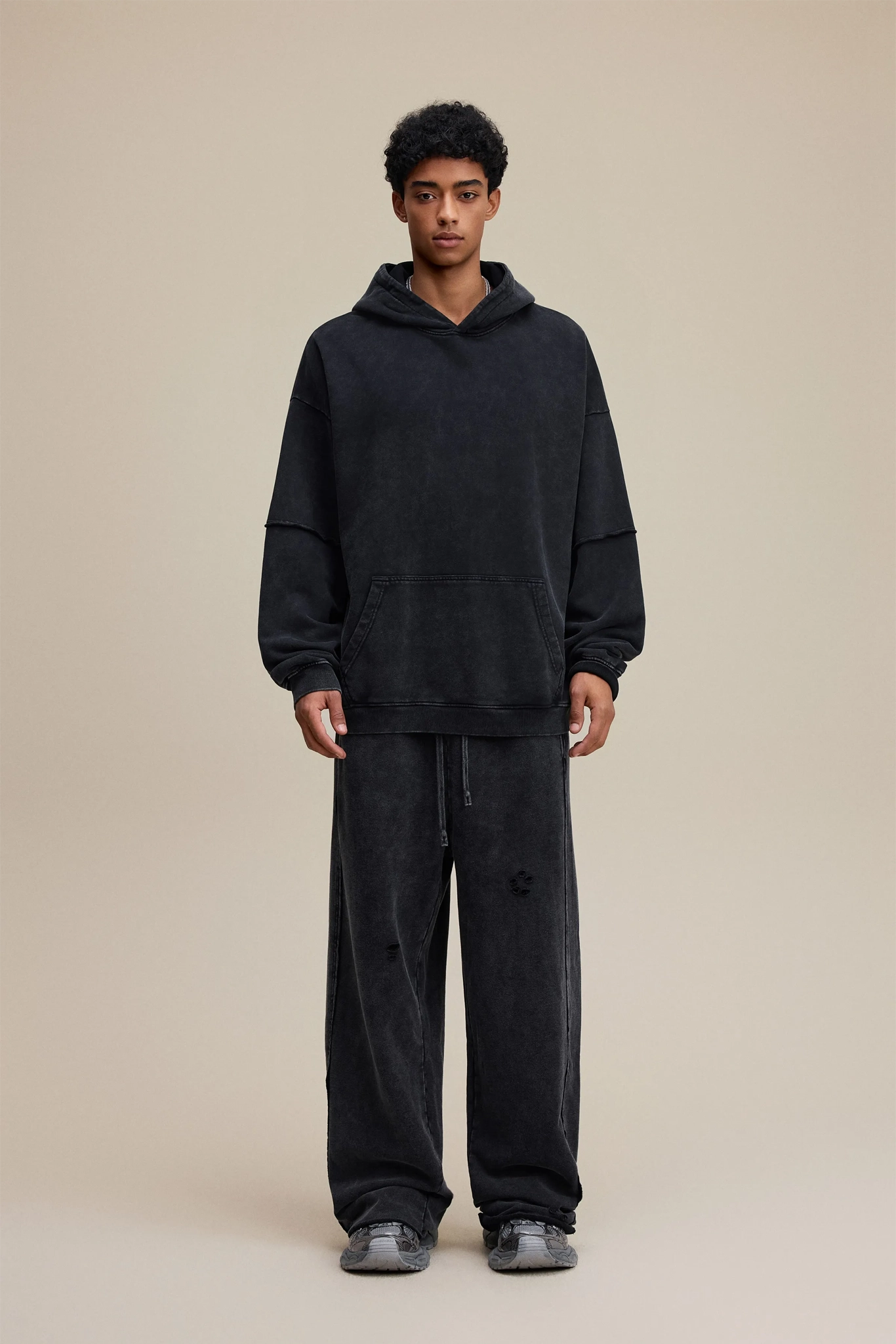 Person wearing a black hoodie and pants on a beige background