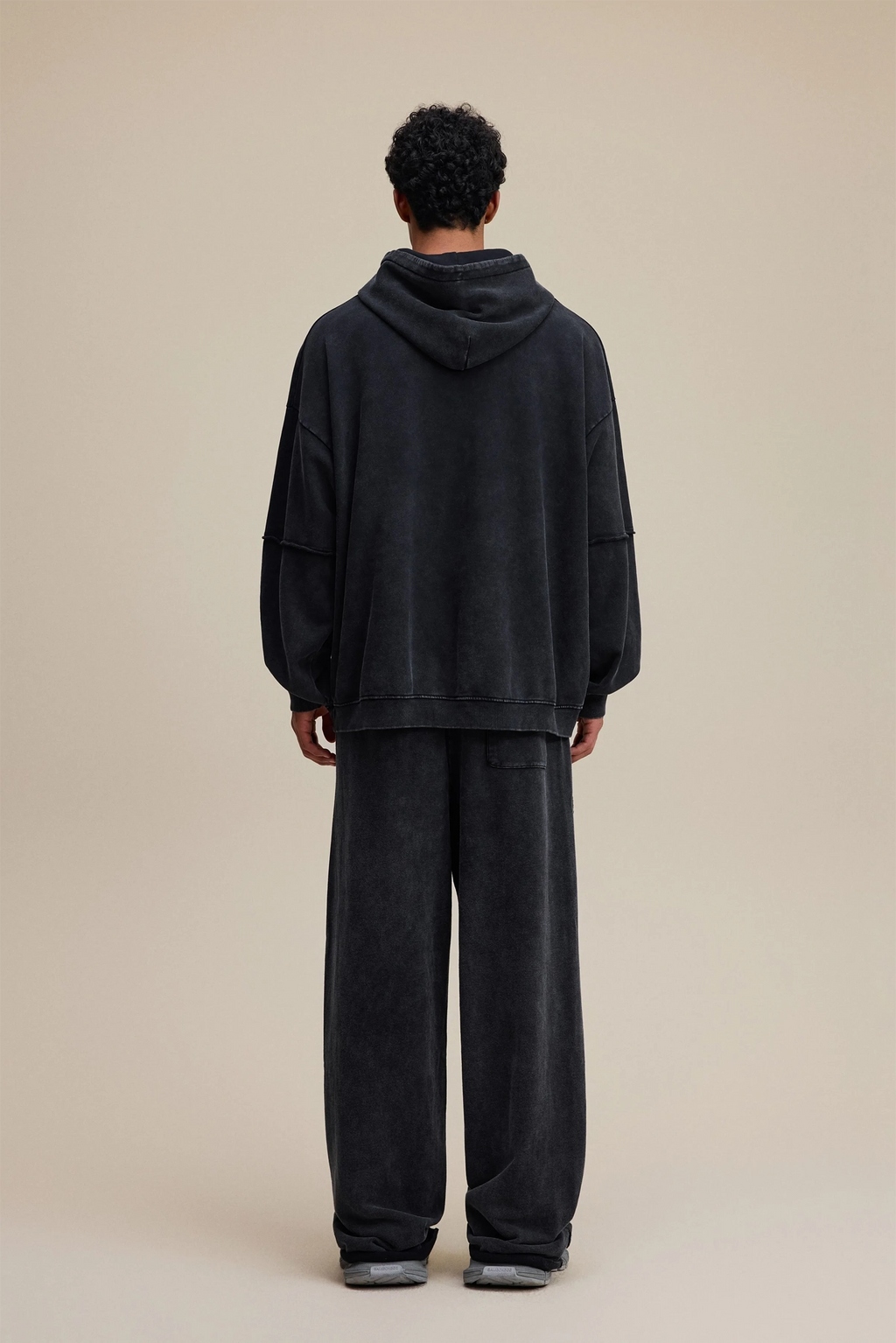 Person wearing a black hoodie and pants set on a beige background