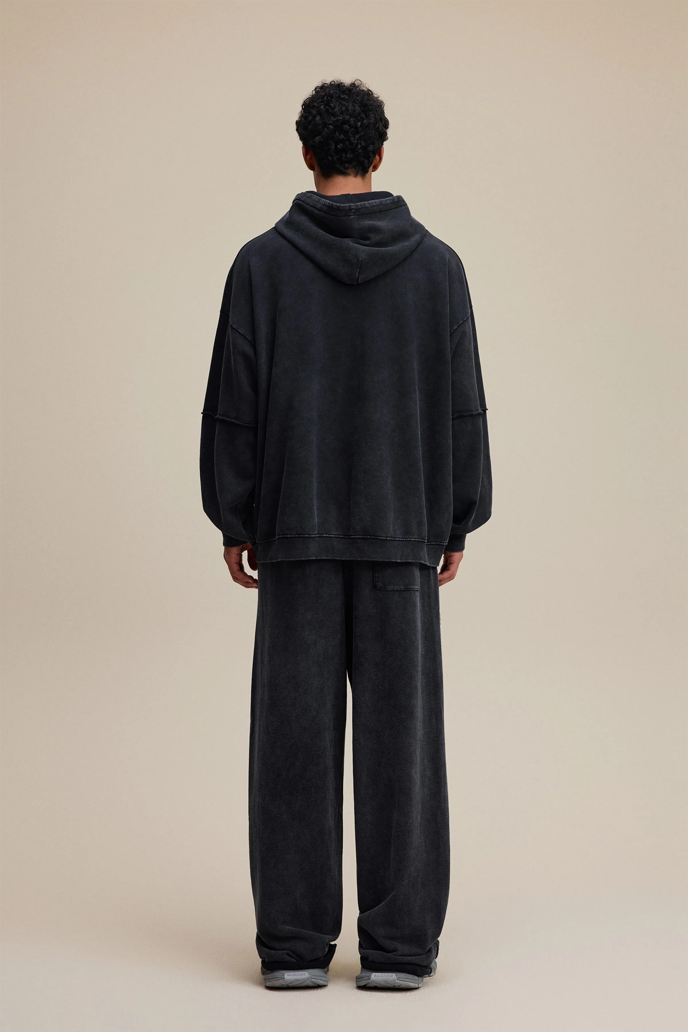 Person wearing a black hoodie and pants set on a beige background