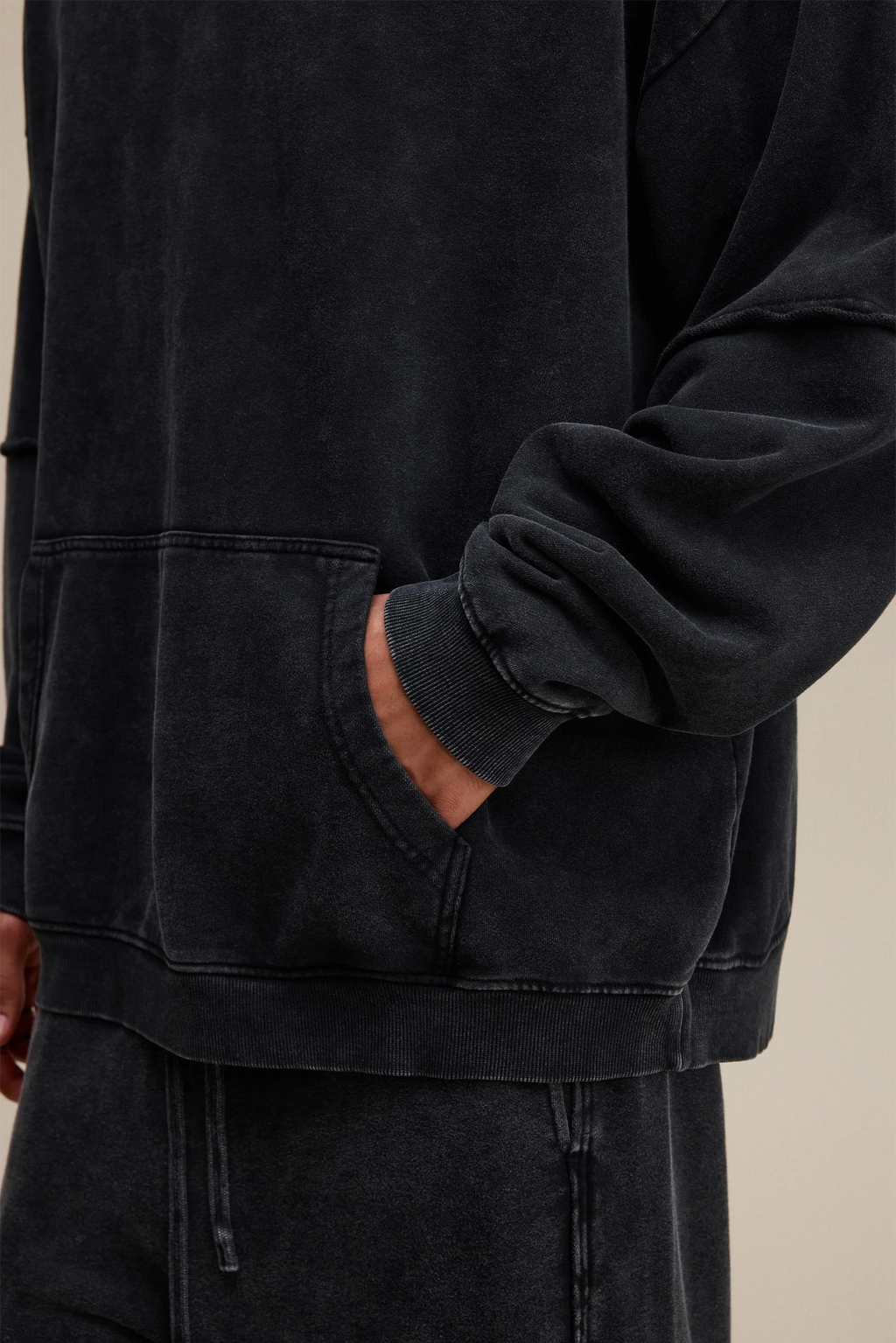 Person wearing a black jacket with a pocket on a beige background