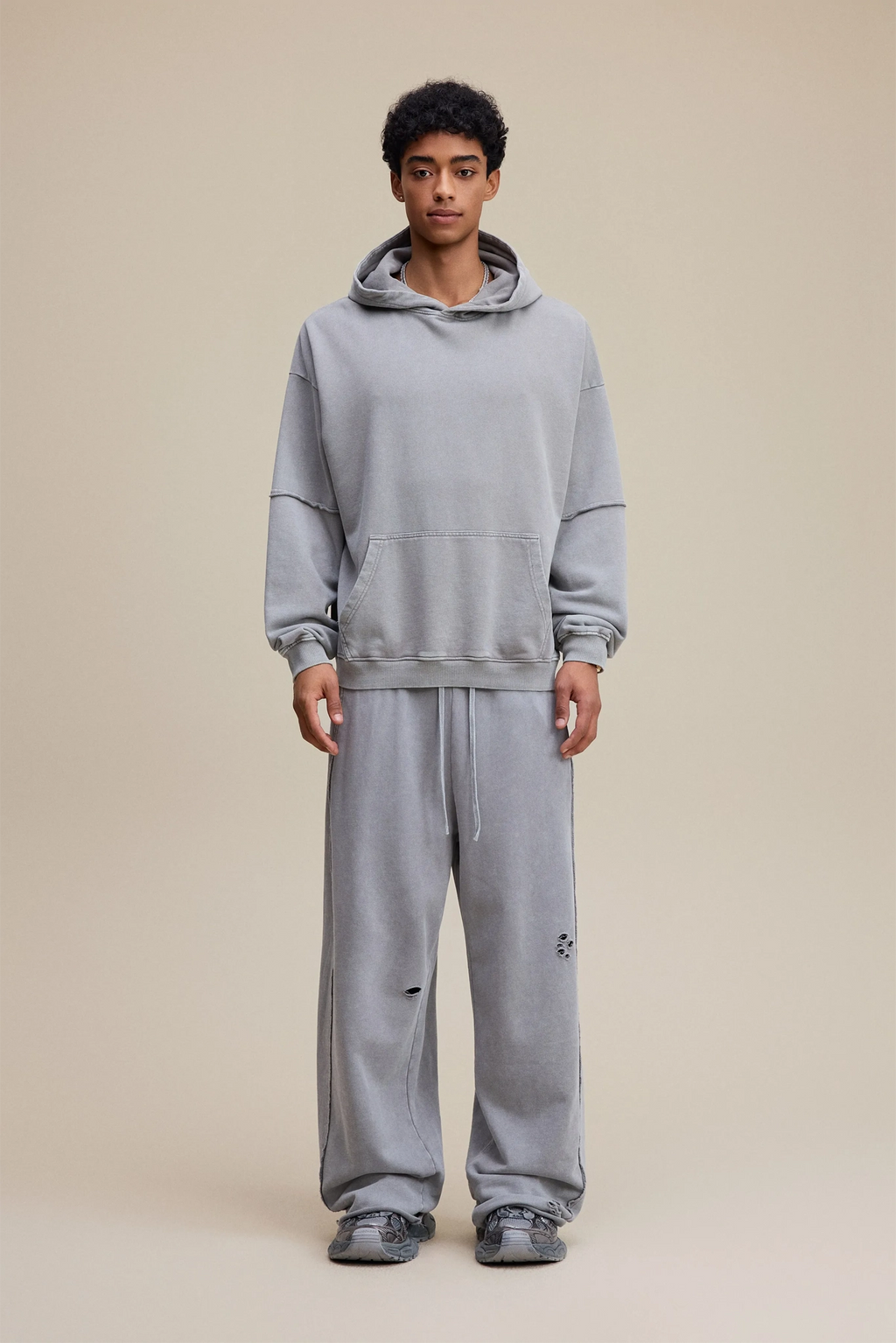 Person wearing a gray hoodie and pants on a beige background