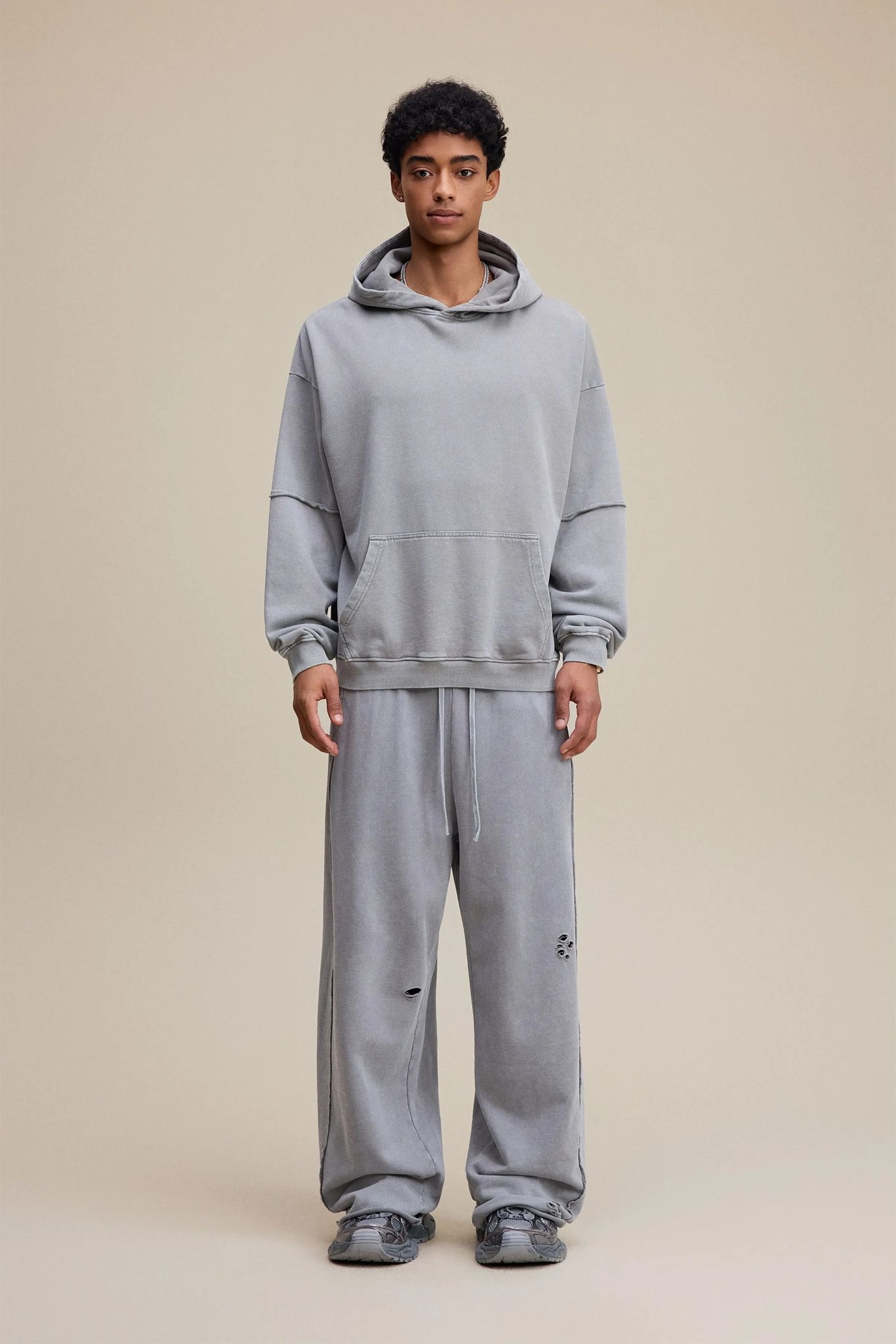 Person wearing a gray hoodie and pants on a beige background