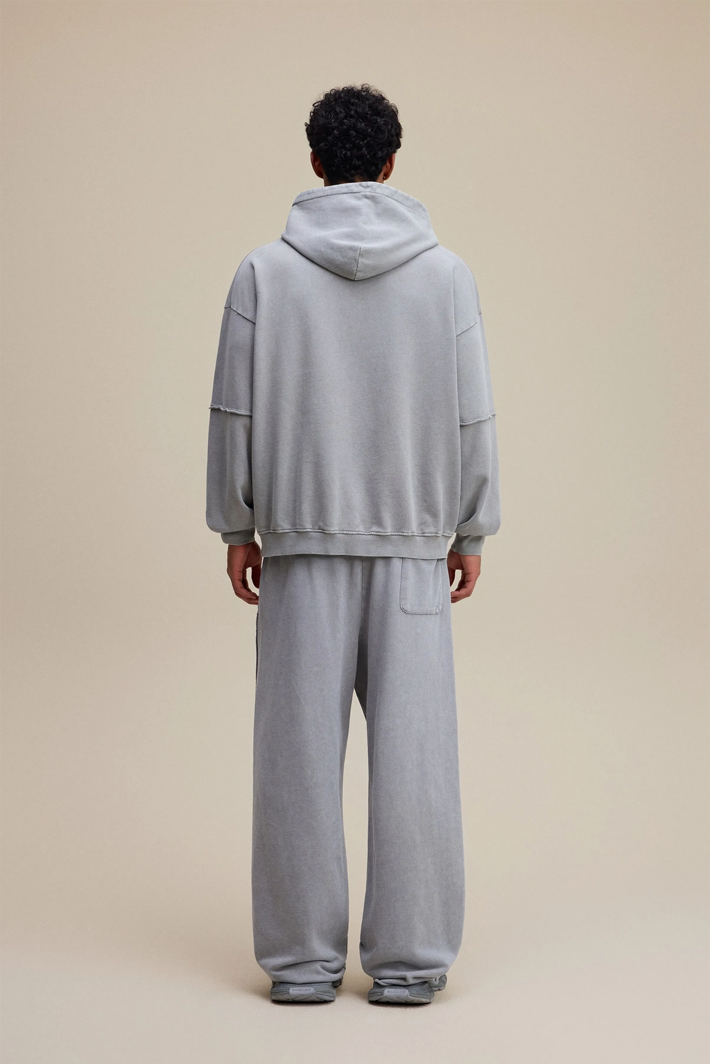 Person wearing a gray tracksuit standing against a beige background