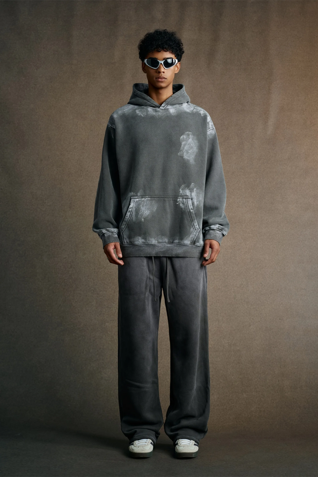 Person wearing a gray hoodie and pants on a brown background