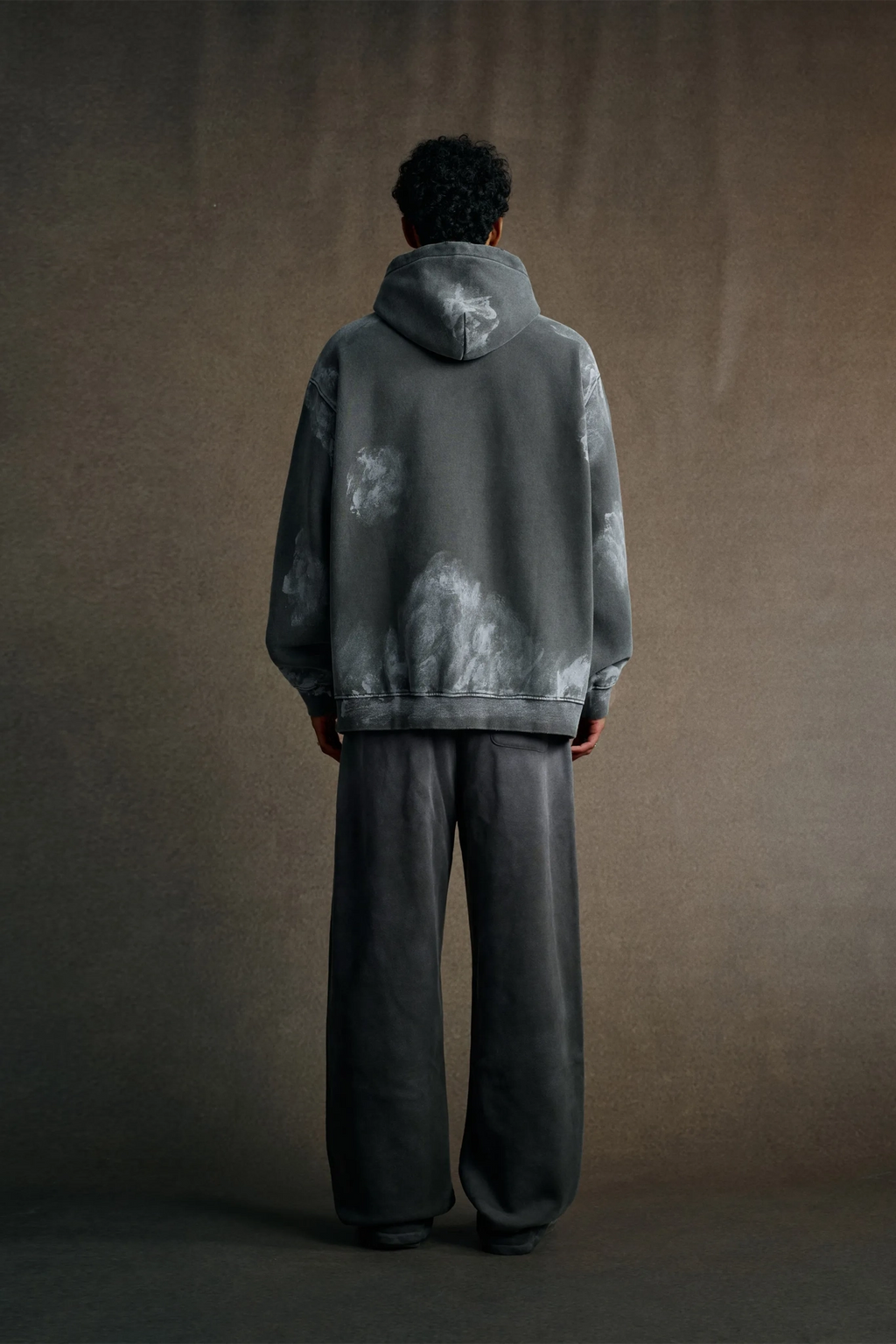 Person wearing a gray tie-dye hoodie and pants against a brown background