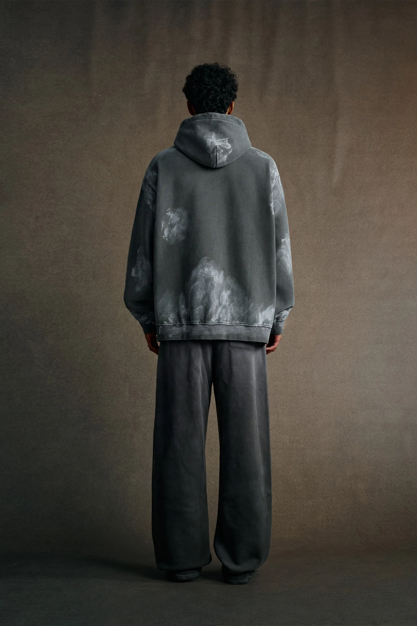 Person wearing a gray tie-dye hoodie and pants against a brown background