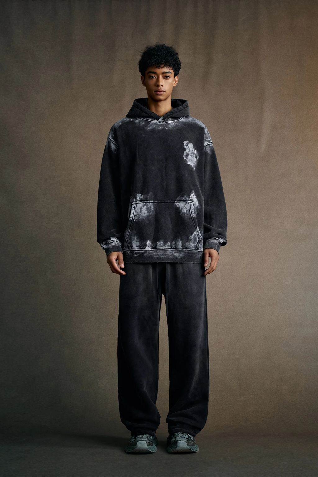 Person wearing a black tie-dye hoodie and pants on a brown background