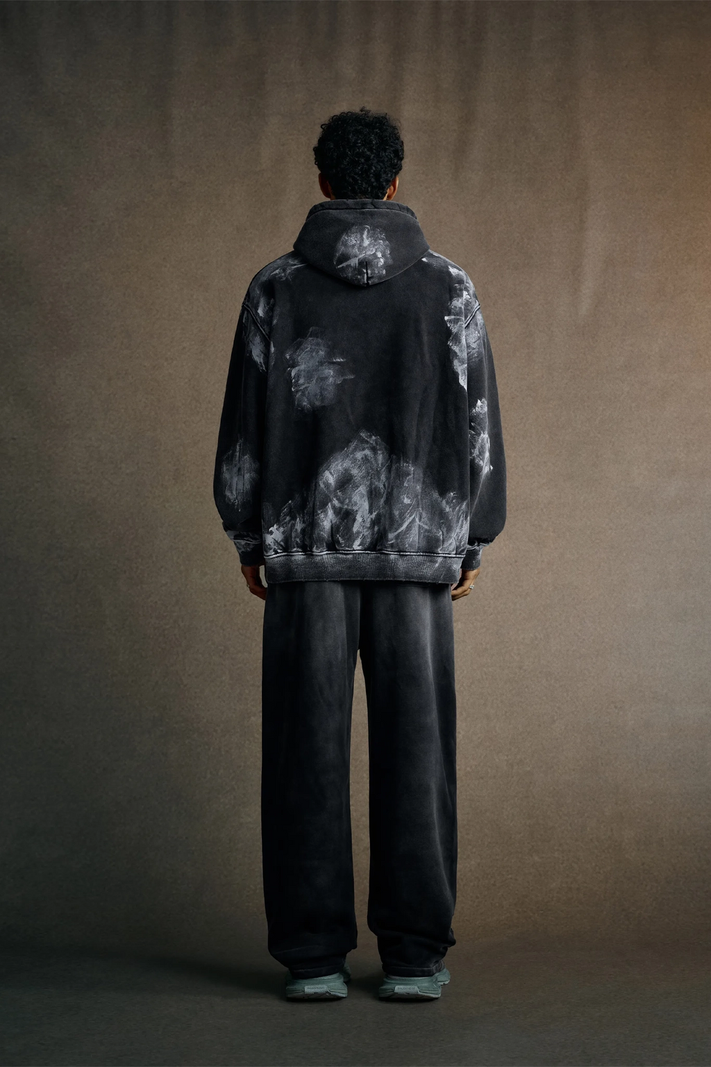 Person wearing a black and gray tie-dye hoodie and pants against a brown background