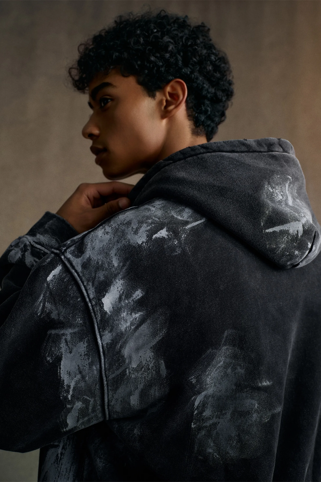 Person wearing a dark gray hoodie with a subtle pattern against a neutral background