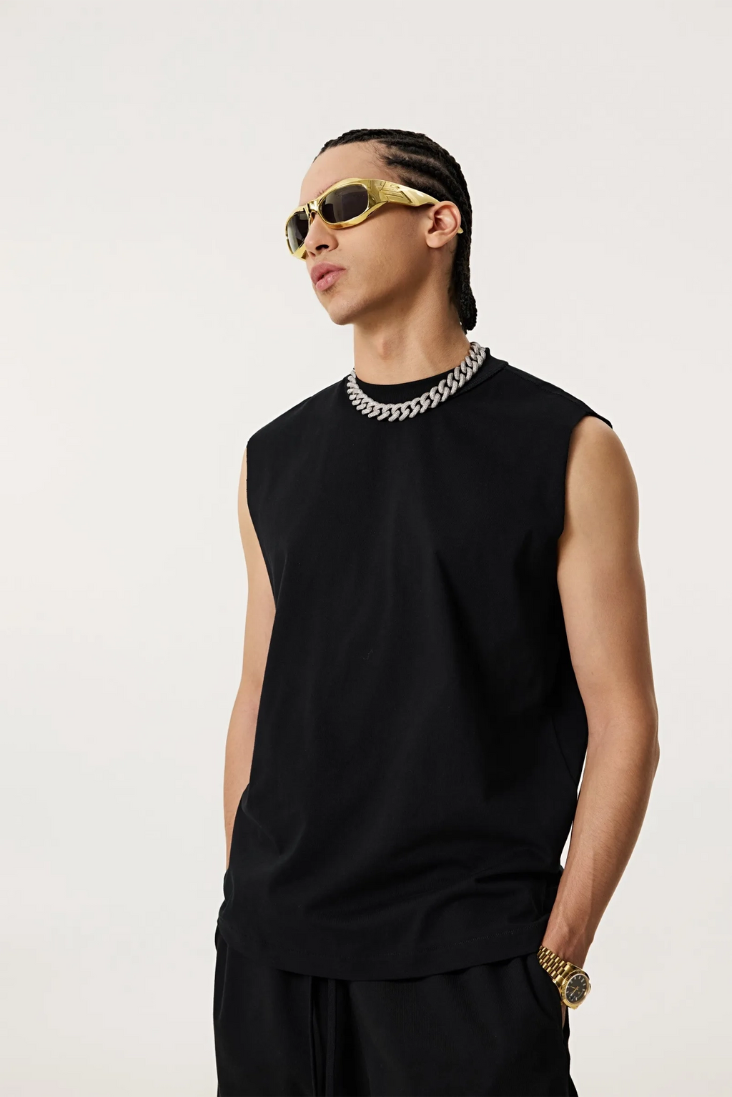 Person wearing a black sleeveless shirt and gold sunglasses on a white background