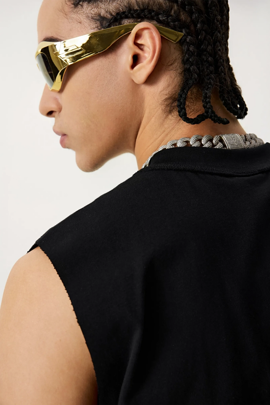 Person wearing gold sunglasses and a black sleeveless top on a white background