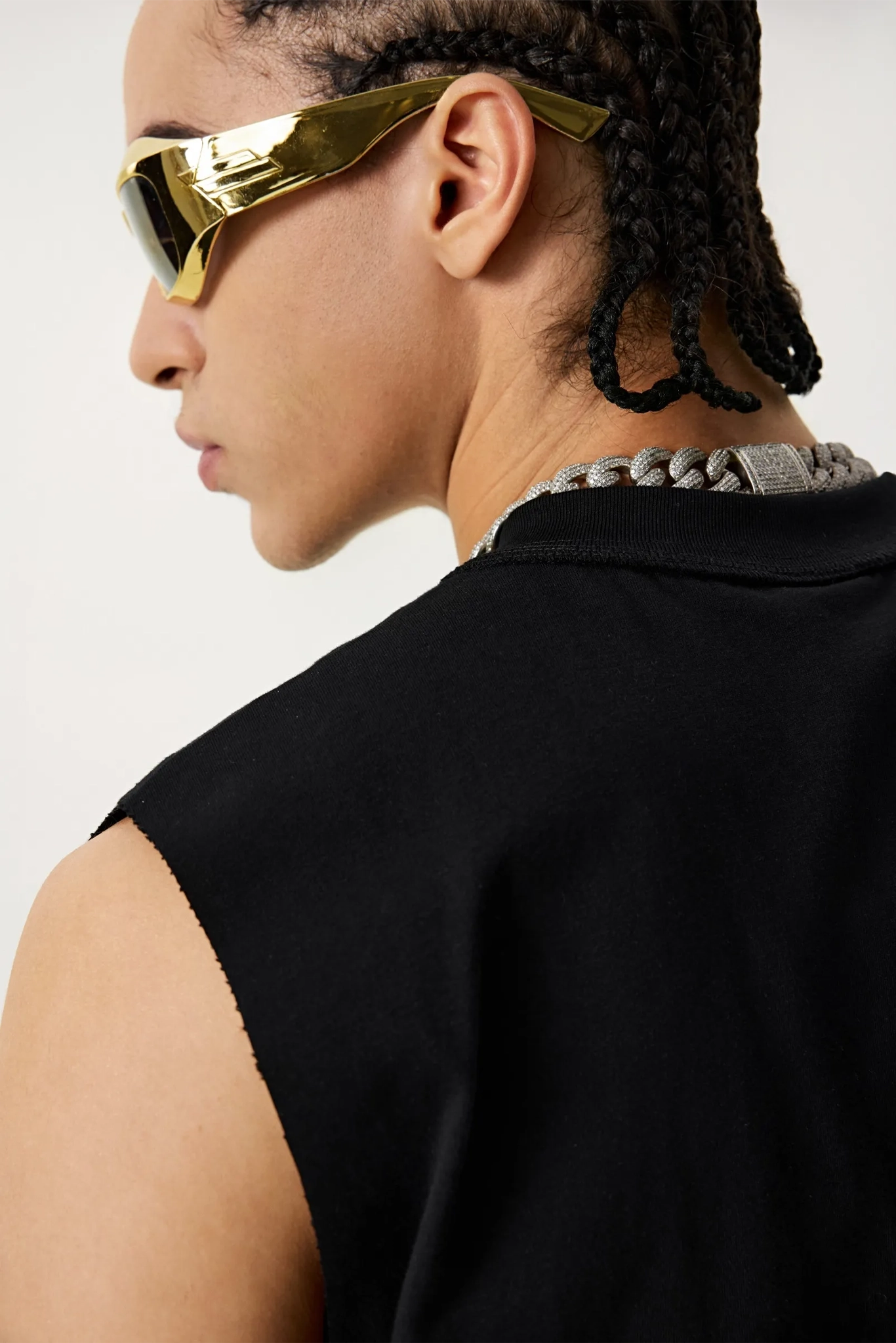 Person wearing gold sunglasses and a black sleeveless top on a white background