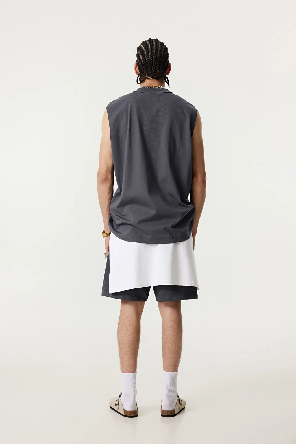 Person wearing a sleeveless dark gray shirt and white shorts on a white background