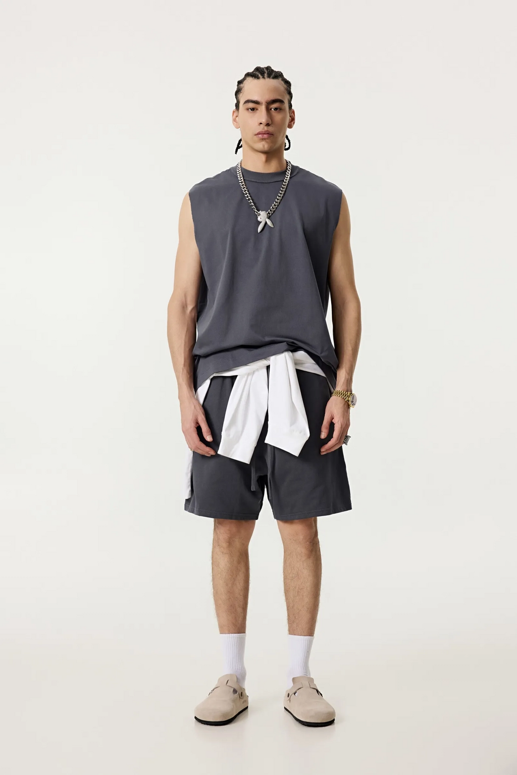 Person wearing a sleeveless gray top, dark shorts, and white socks on a plain background